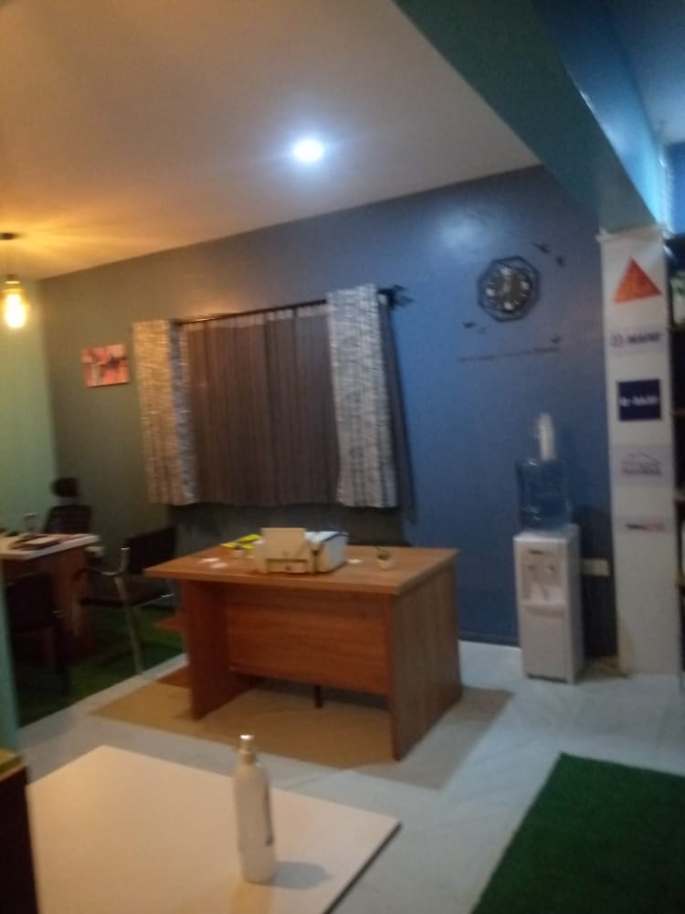 Office space with a wooden desk, chair, window with curtains, wall clock, and water dispenser in the corner.