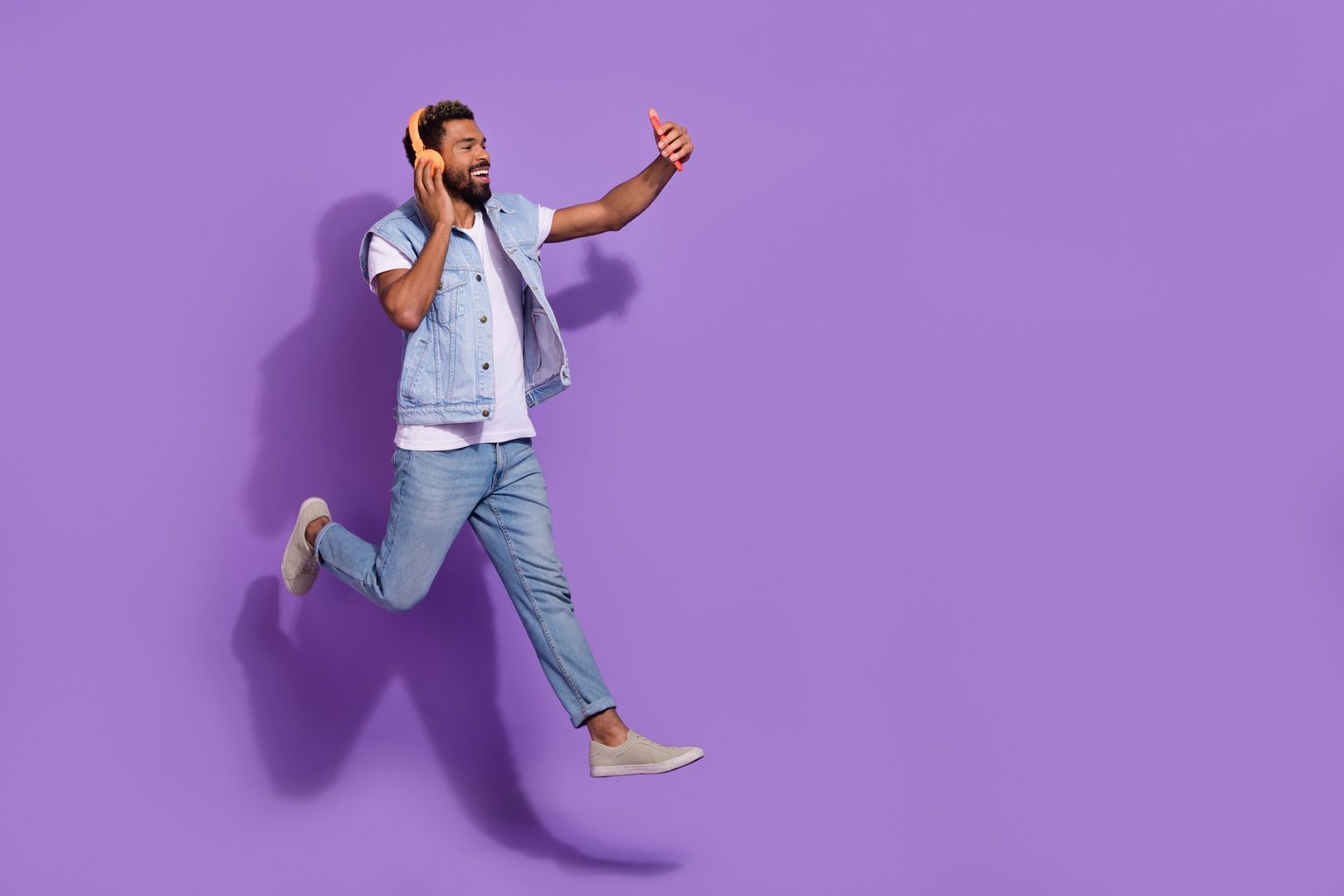 Full length photo of cheerful positive man wear jeans jumping empty space recording self video isolated violet color background.