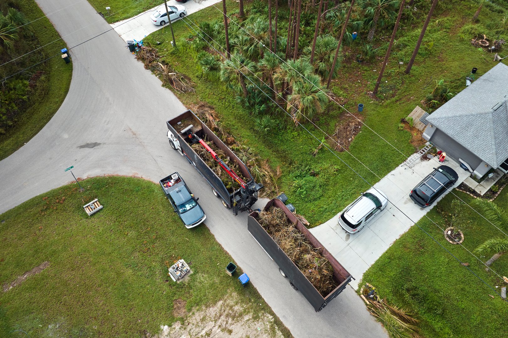 Top view of Hurricane Ian special aftermath recovery dump truck picking up tree branches debris from Florida rural streets. Dealing with consequences of natural disaster.