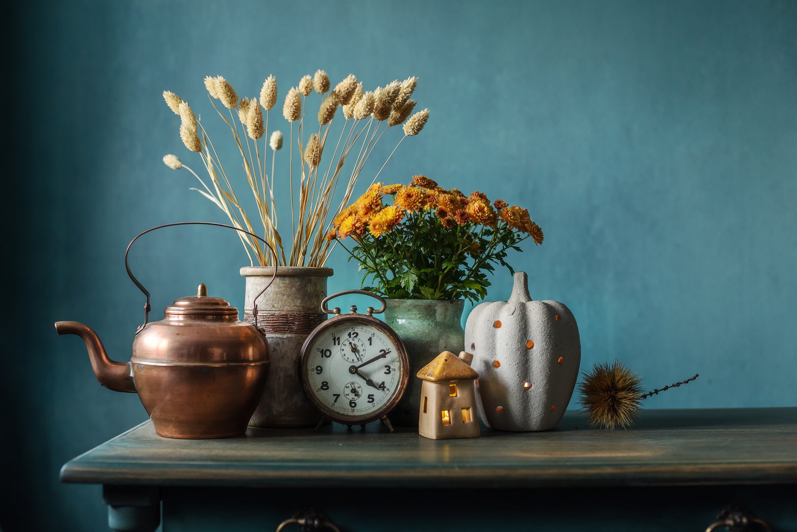 Autumn still life in the kitchen with an antique alarm clock, a copper kettle, a bouquet of chrysanthemums and a decorative pumpkin with a candle.. Cozy home decor concept in vintage rustic style for thanksgiving