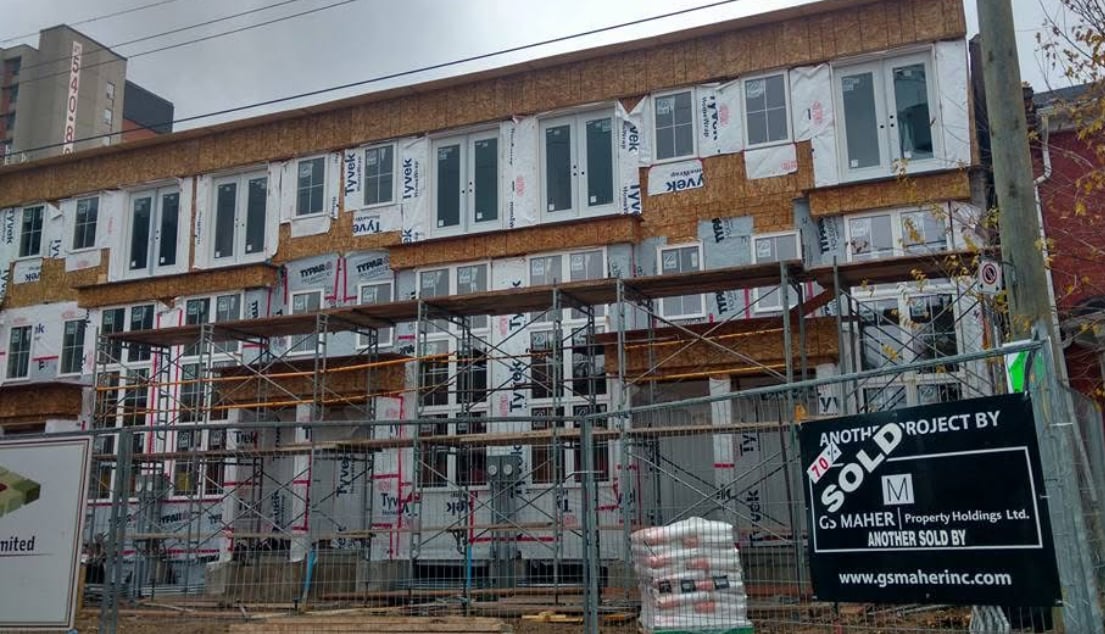 Construction site with scaffolding in front of a building under development, featuring numerous doors and windows installed.