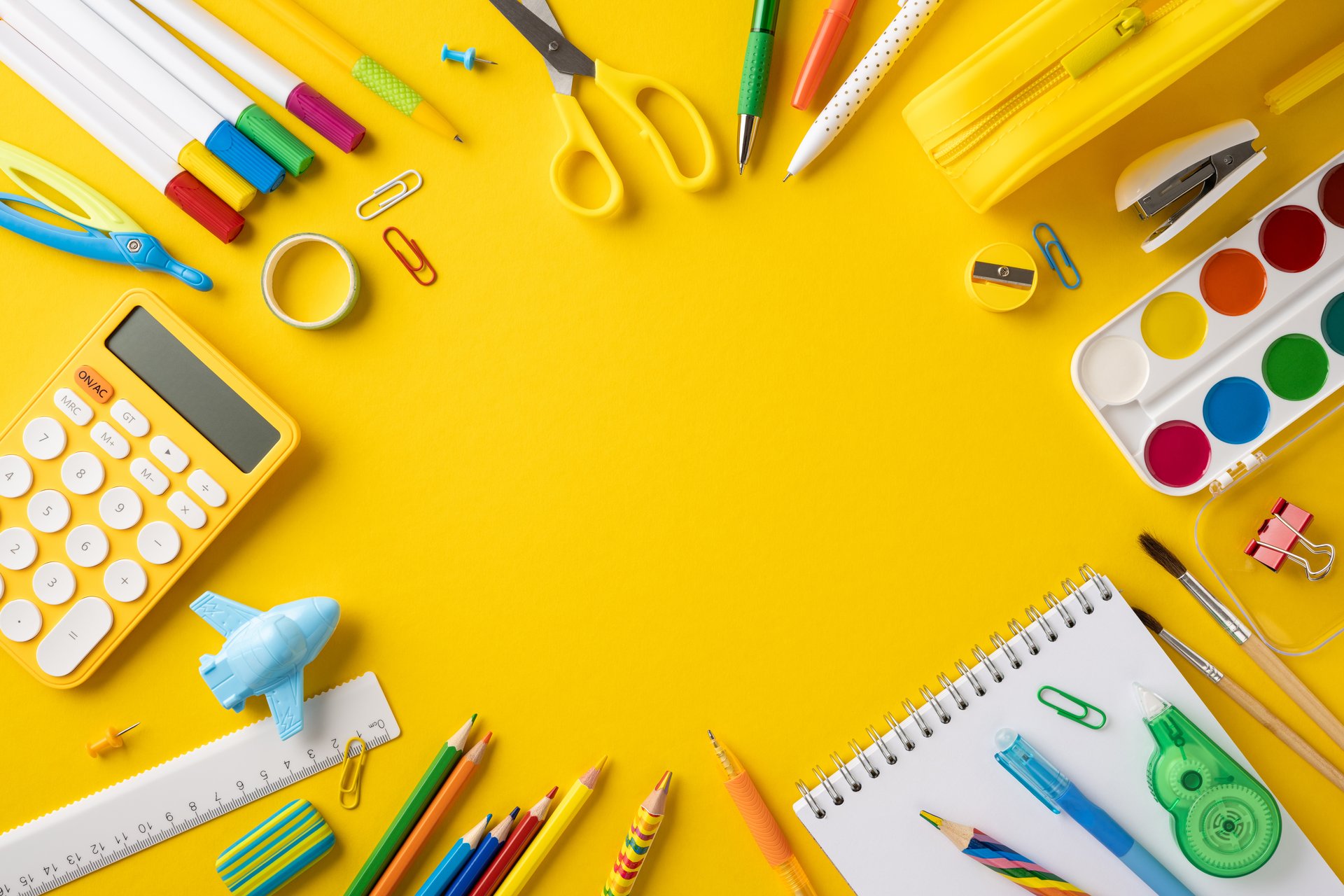 Artistic flat lay of various stationery items including pens, pencils, scissors, and calculators, set against a vibrant yellow backdrop, providing an energetic and cheerful atmosphere for creativity