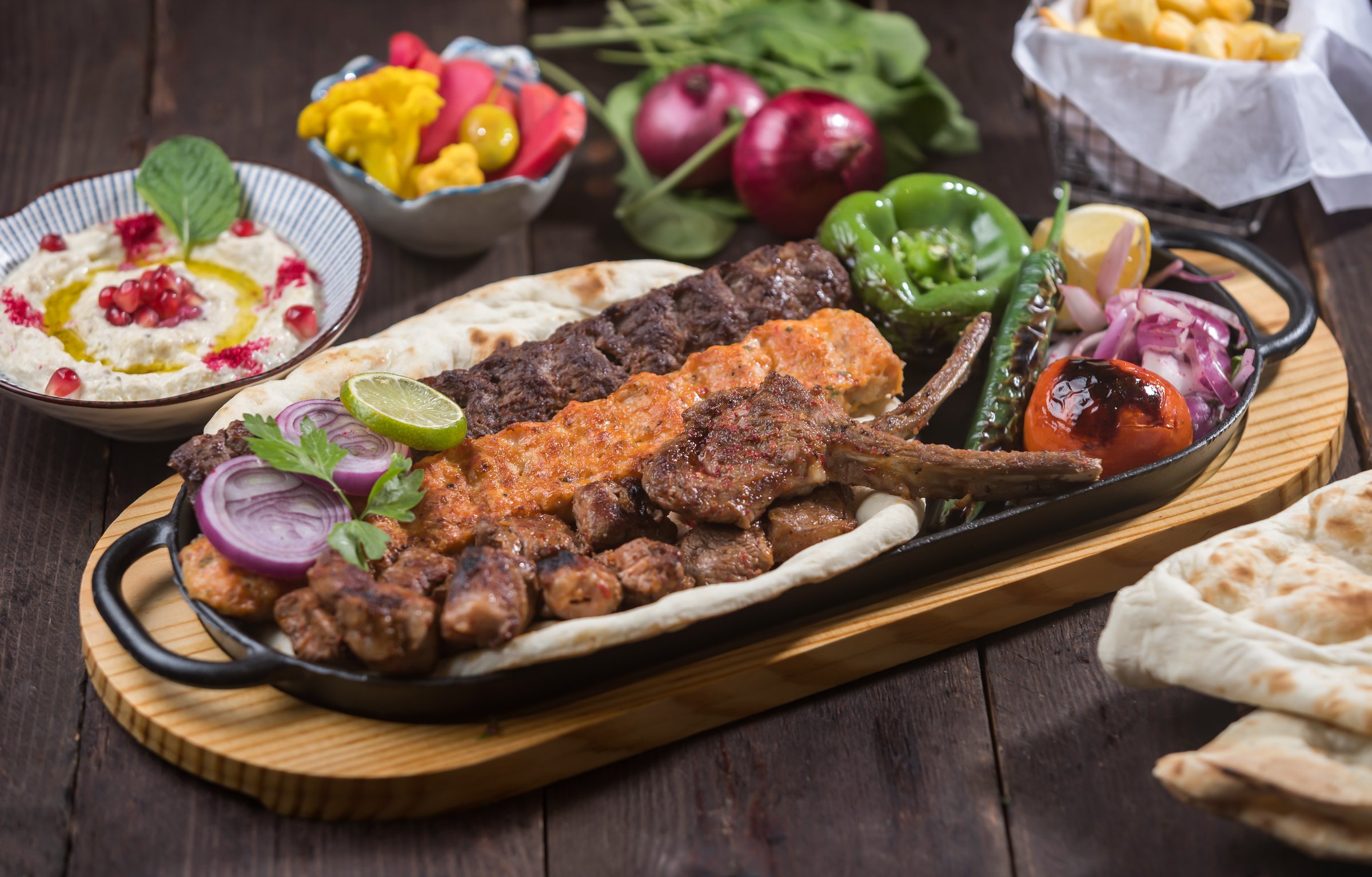 Mixed Grill Platter served in tray with meat kebab, chicken kabab, tikka, boti, lamb chops, pita bread, hummus, and salad isolated on wooden table side view of Middle Eastern bbq