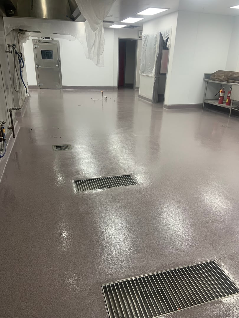 Clean industrial kitchen with stainless steel appliances, ceiling vents, and a shiny, wet floor.