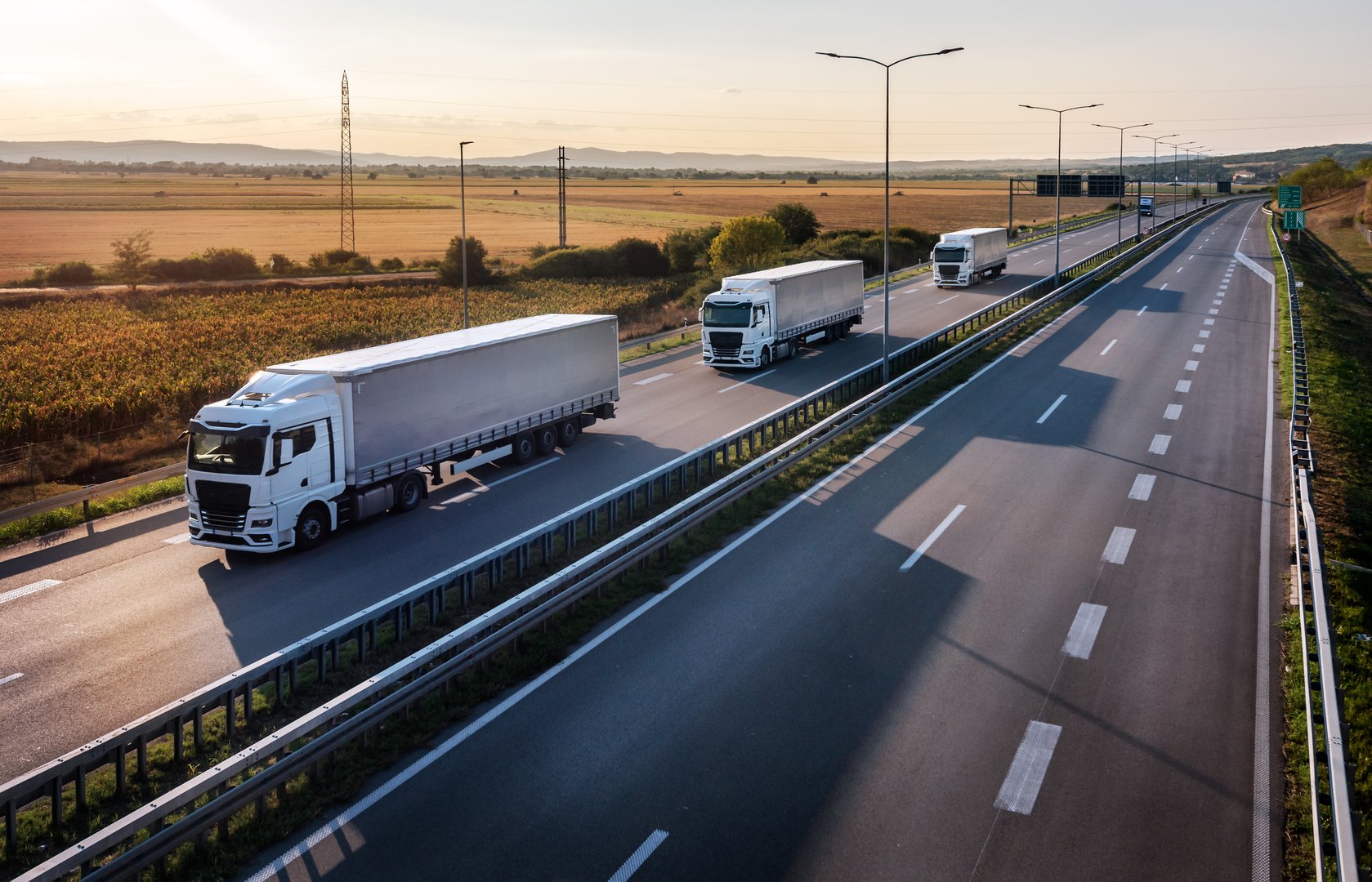 Caravan or convoy of white trucks in line on a country highway at sunset