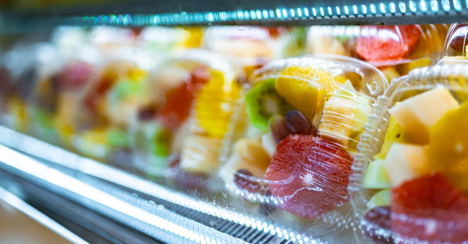 Plastic boxes with fresh fruits displayed in a commercial refrigerator. Fruit salad