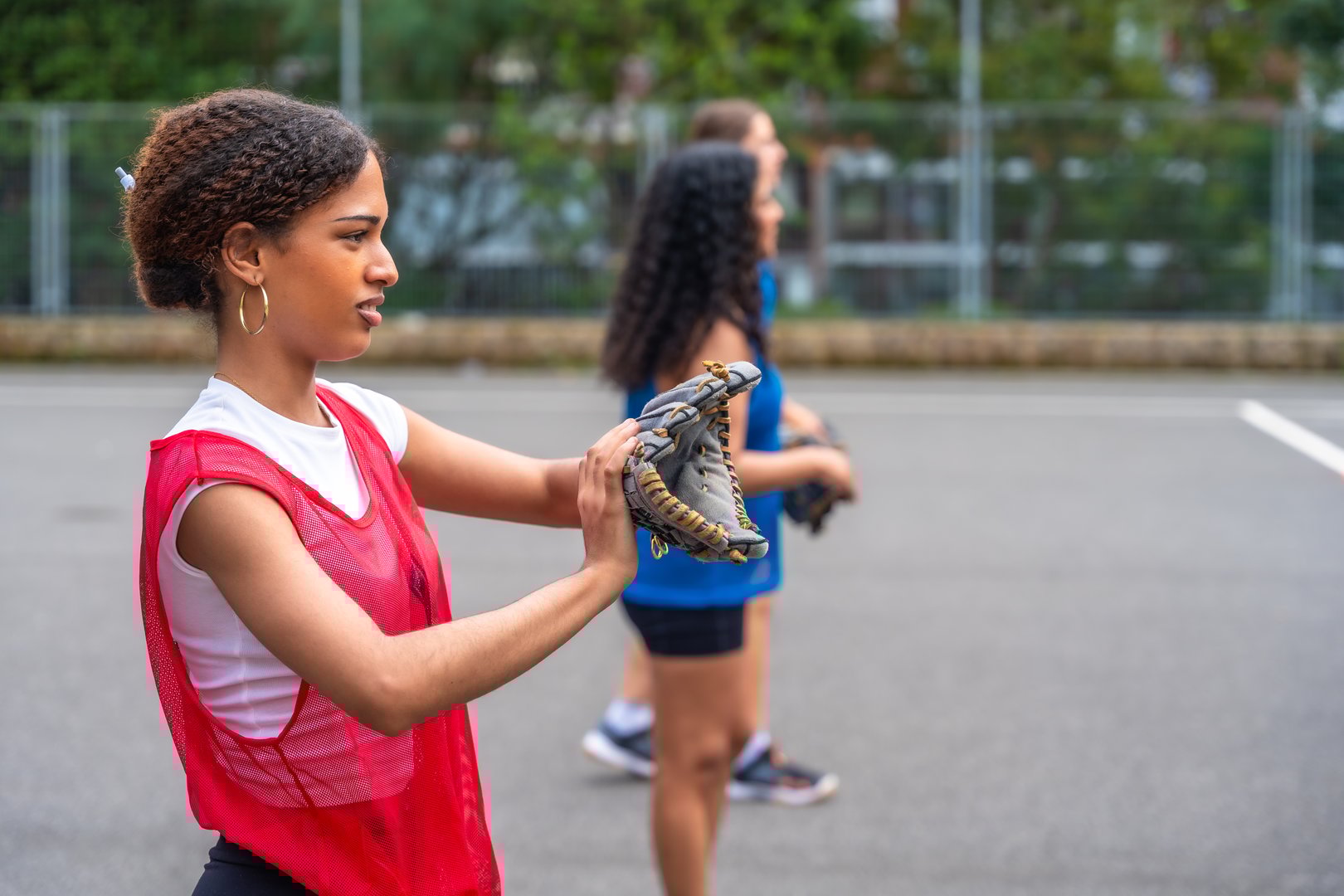 Young female baseball player adjusting her glove while teammates wait patiently for their turn during an outdoor practice session on the baseball field, embracing teamwork and skill development