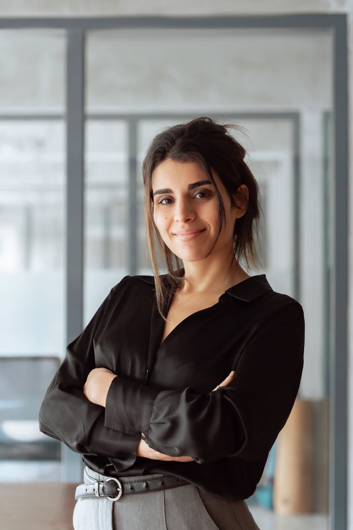 Vertical portrait of smiling latin hispanic business woman employee with crossed arms looking at camera. European or eastern confident 30s middle age female leader businesswoman standing in office