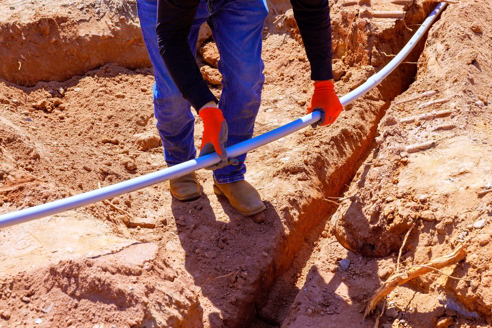 Construction worker lays electrical pipe in filled trench during foundation work