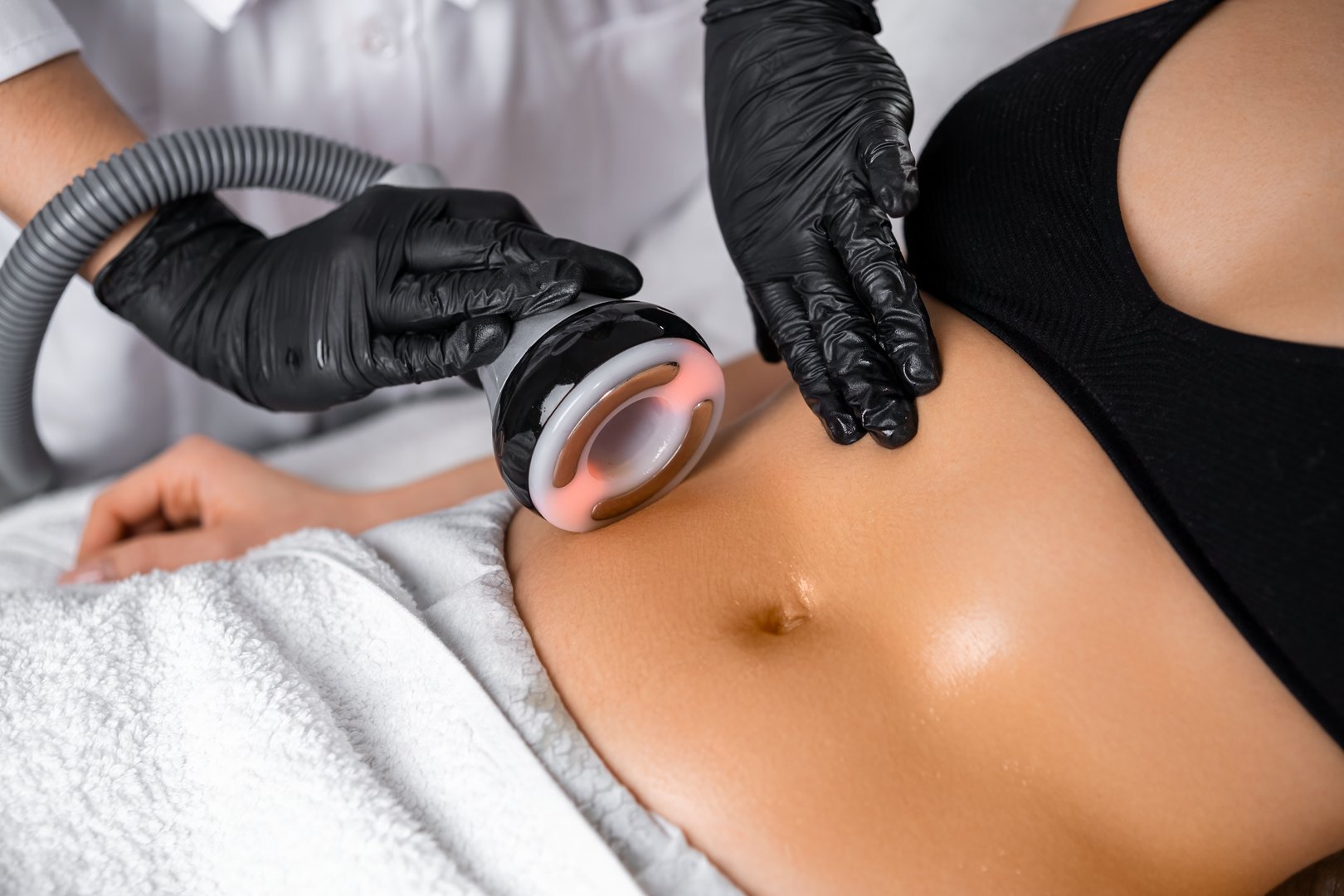 Close cosmetologist using ultrasound device while performing lifting procedure on woman belly.