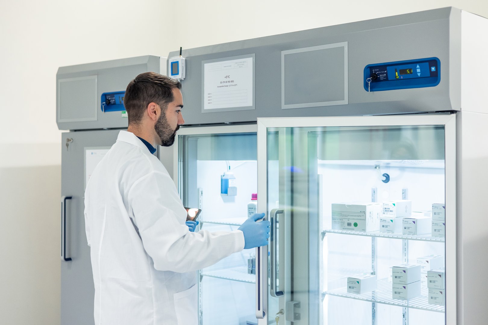 Scientist wearing a lab coat and gloves is opening a refrigerator in a scientific laboratory, containing medicines, vaccines and other pharmaceutical products