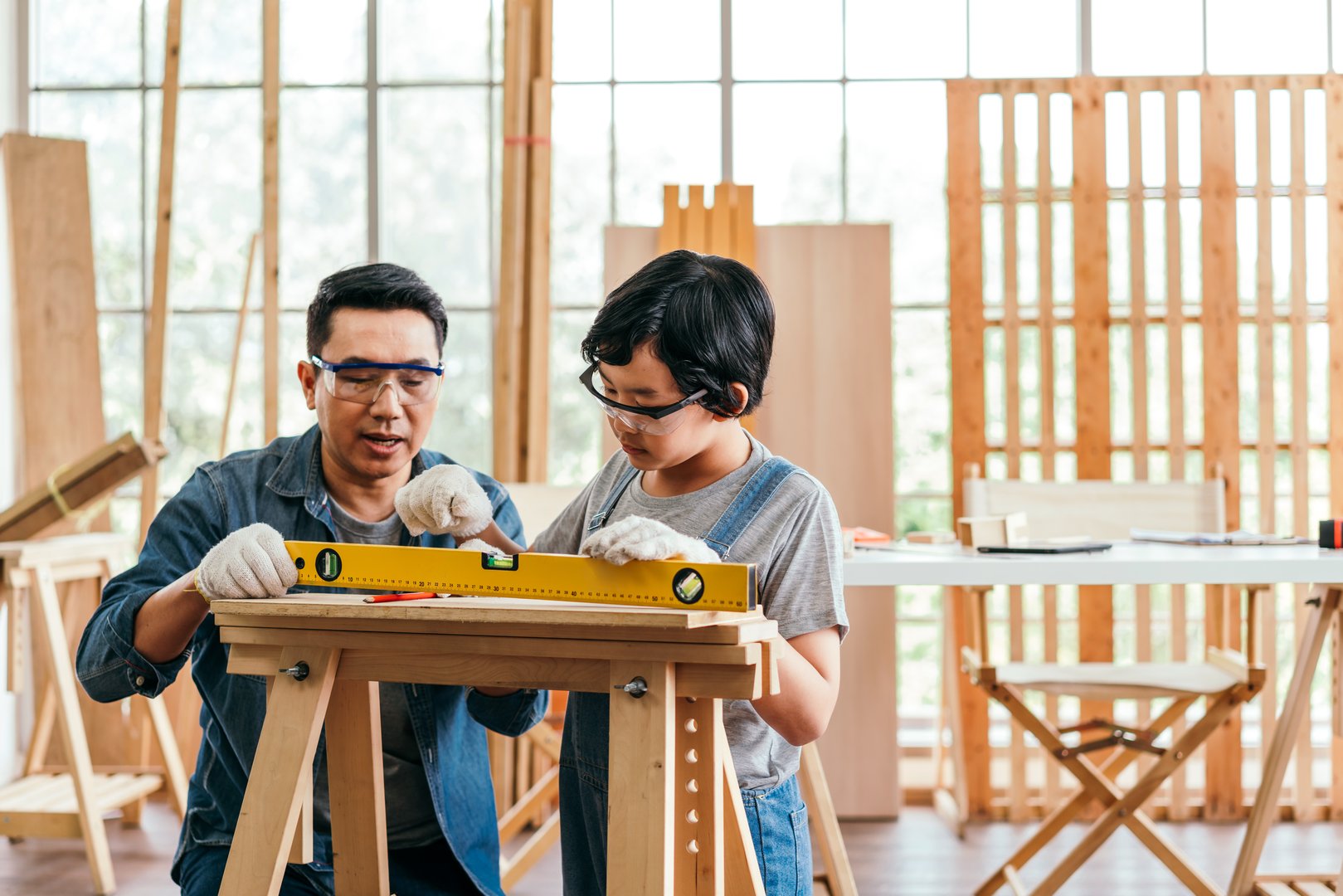 Close-up carpenter hands wearing work gloves draw the cutting line with a pencil on a wooden board. Construction industry, carpentry workshop. Carpenter at work on wooden boards. Carpentry concept.