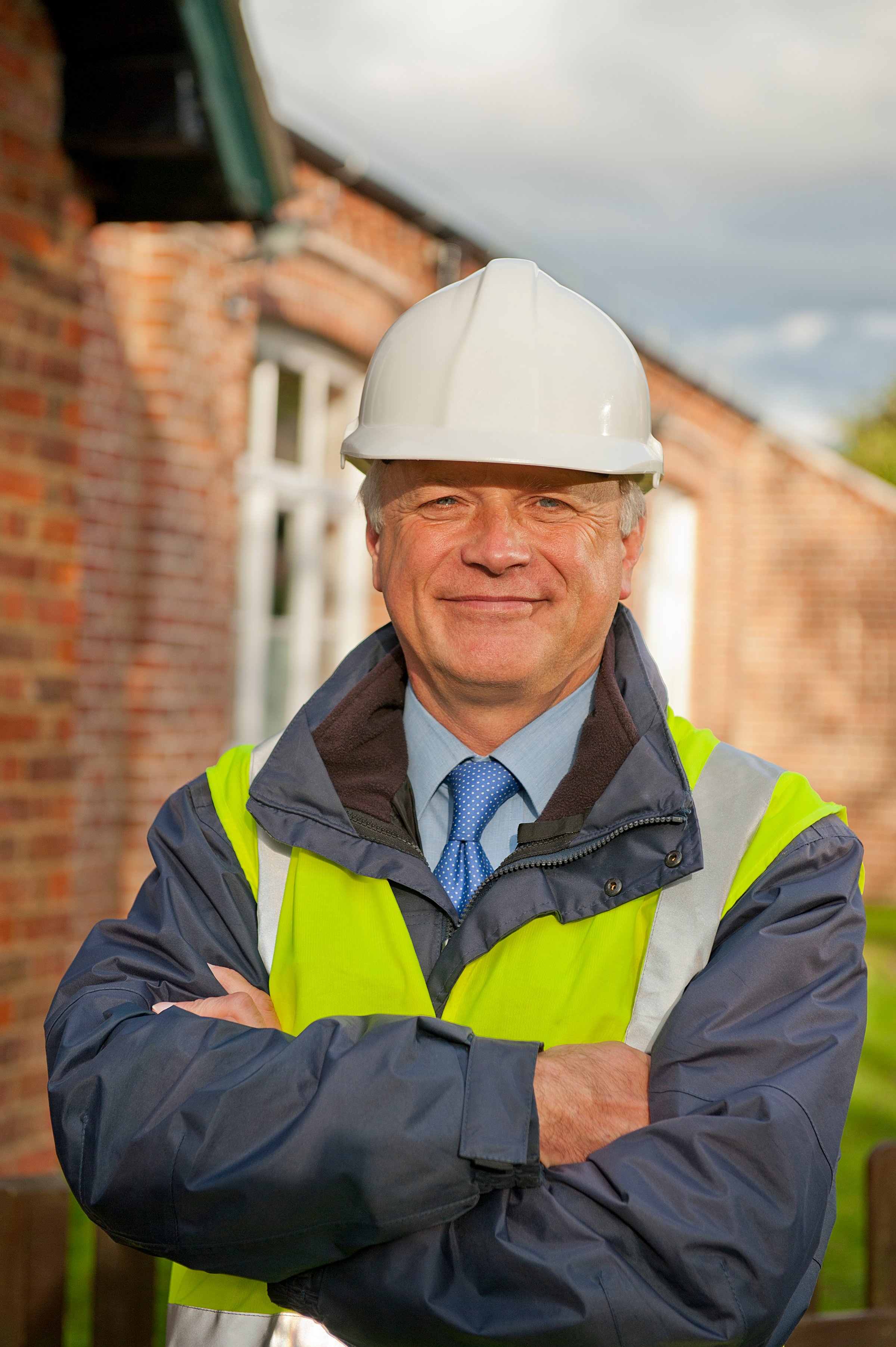 Portrait of a smiling construction engineer, with his arms folded, wearing a white safety helmet and reflective jacket.