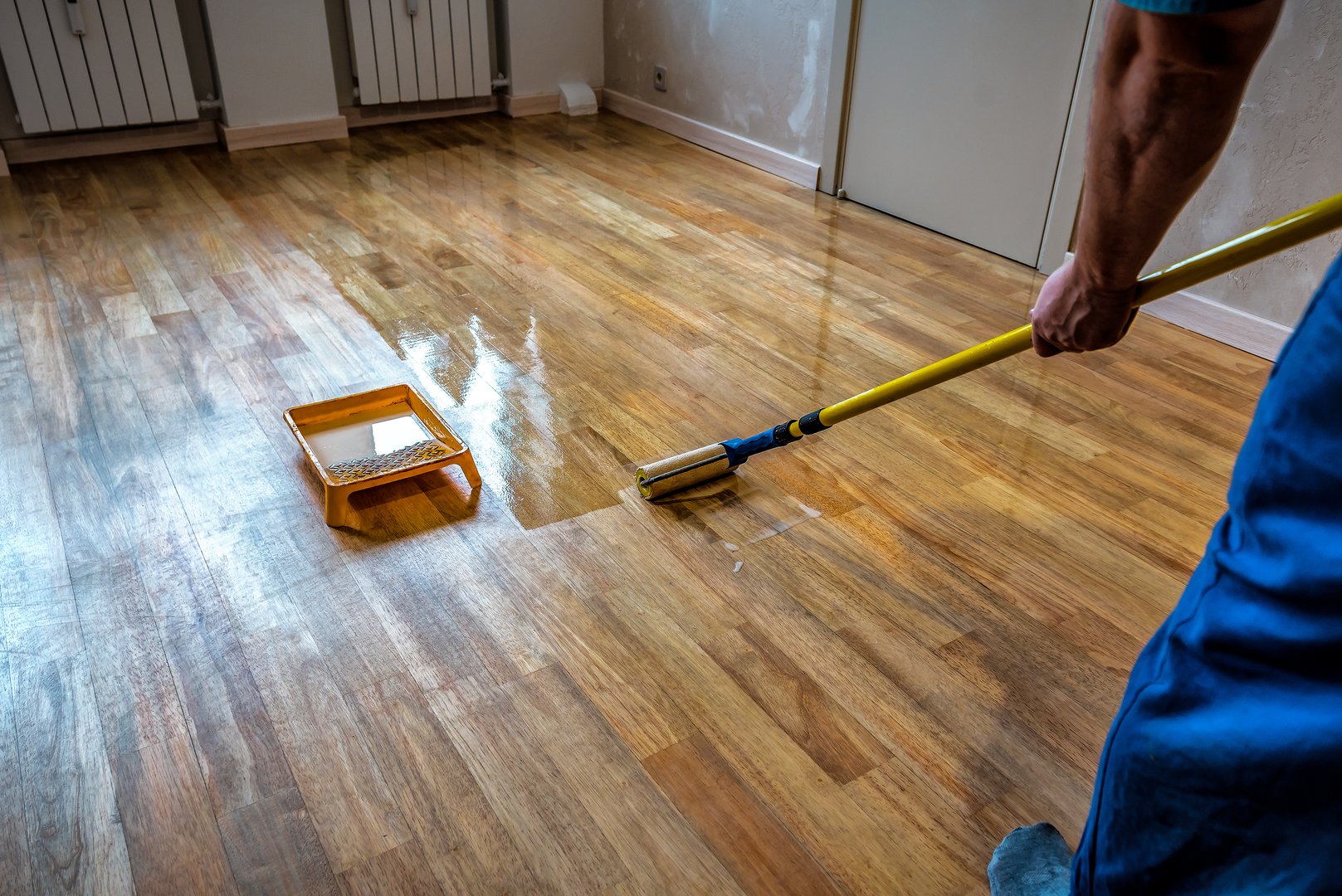 Parquet floor renovation. Lacquering wood floors. Worker uses a roller to coating floors. Industrial theme