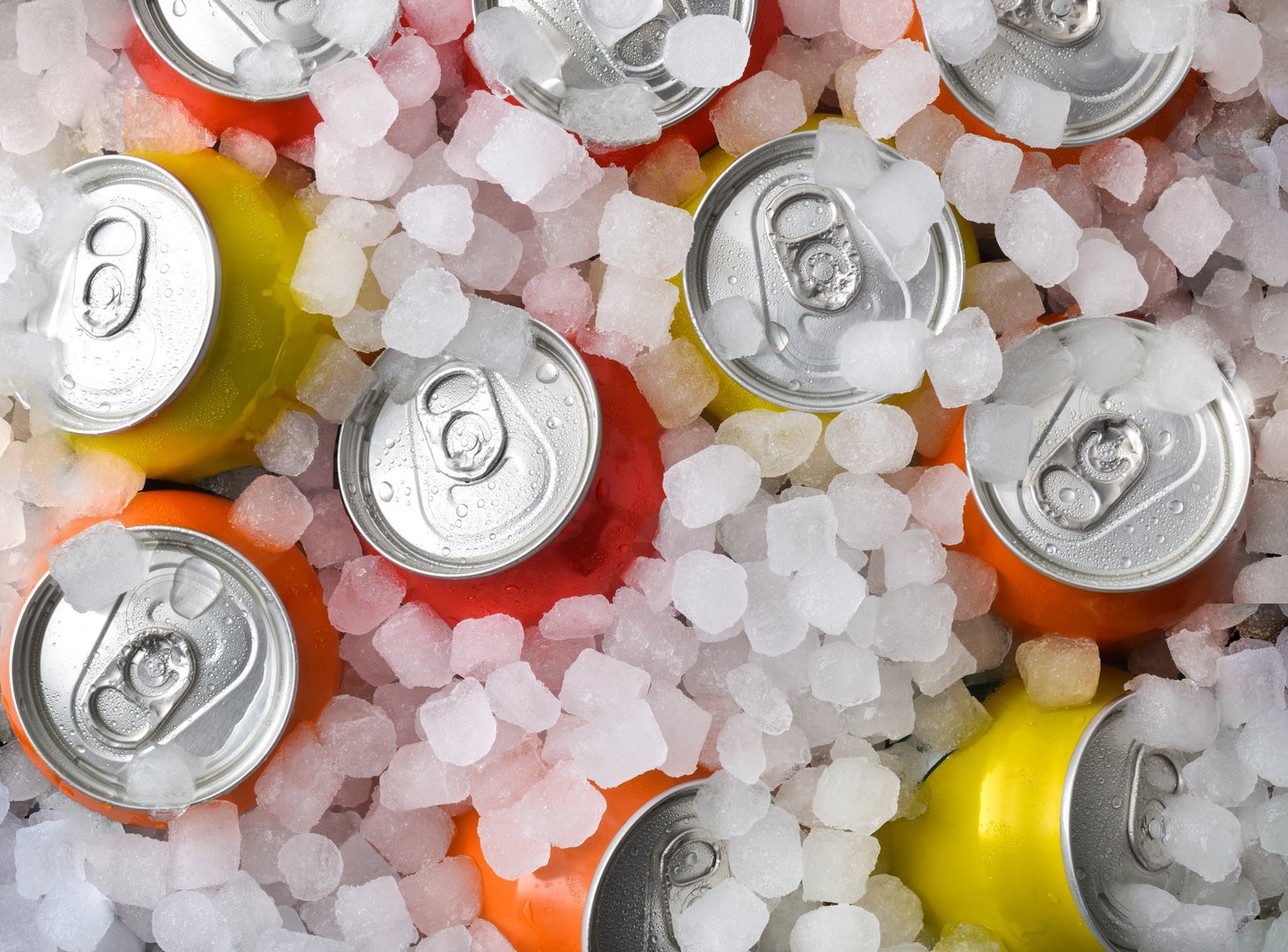 Group of cold orange, yellow, and red drink cans covered in ice. Top view.