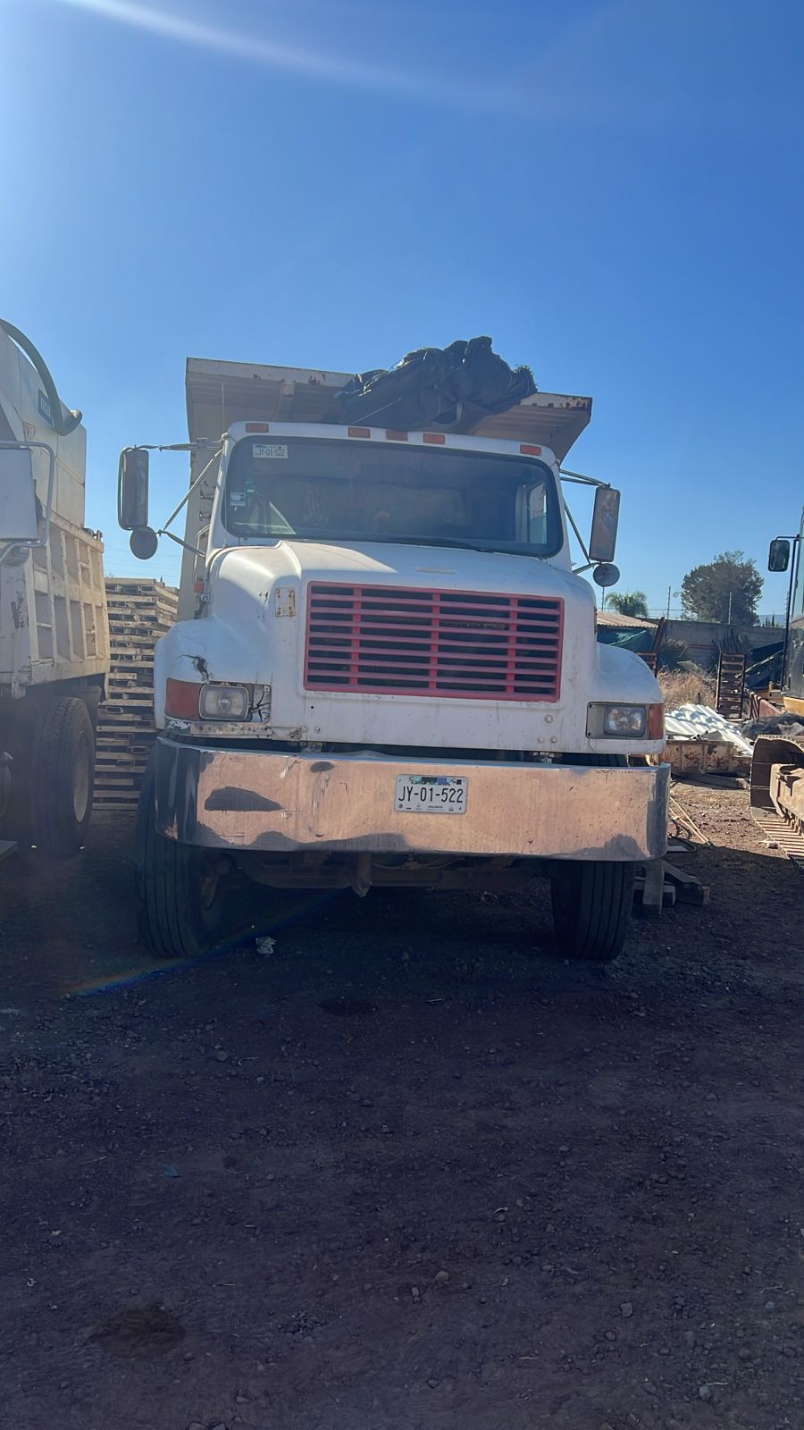 Front view of a white dump truck parked on dirt, with a load of dark material visible in its bed.