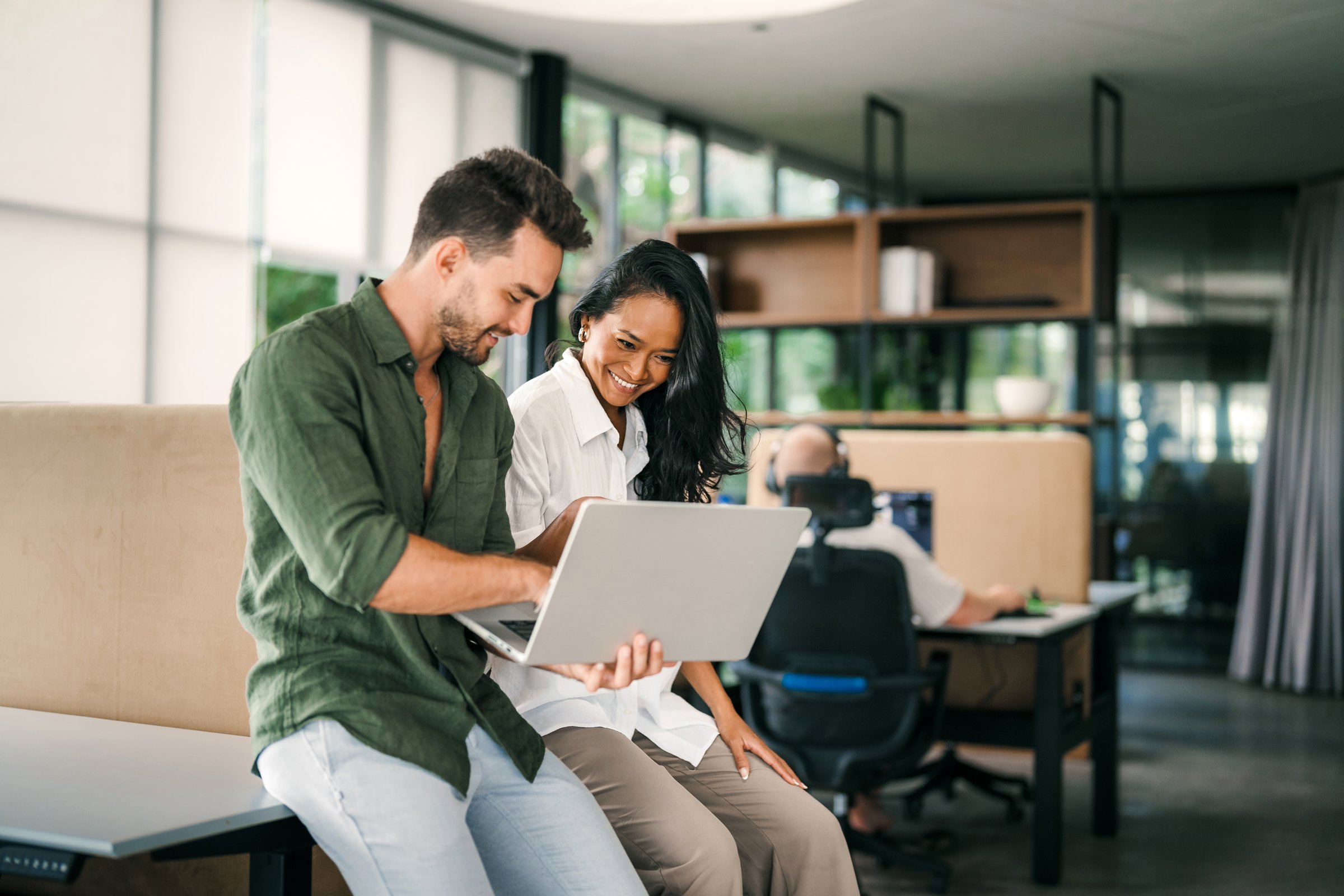 Two happy diverse multiethnic business team people working, talking in corporate office using laptop computer. Busy business man and woman colleagues at workplace.