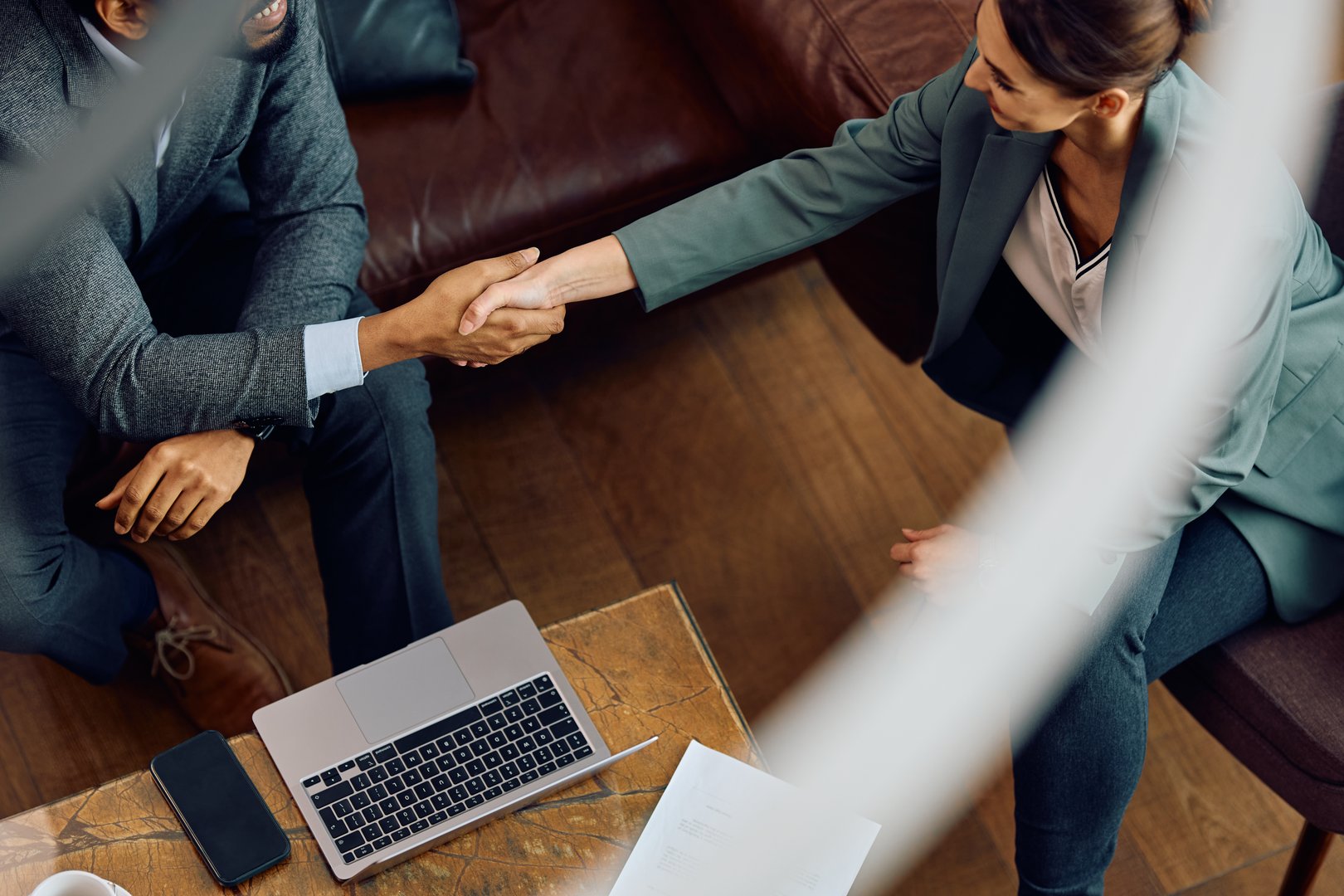 High angle view of coworkers handshaking during business meeting in hotel lobby.