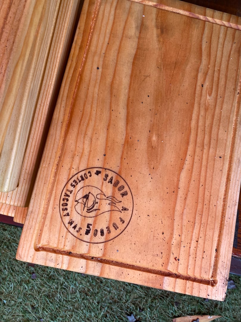 Wooden cutting board with a circular stamp reading "Curtesanos - Sabor a Pueblo" on the surface.