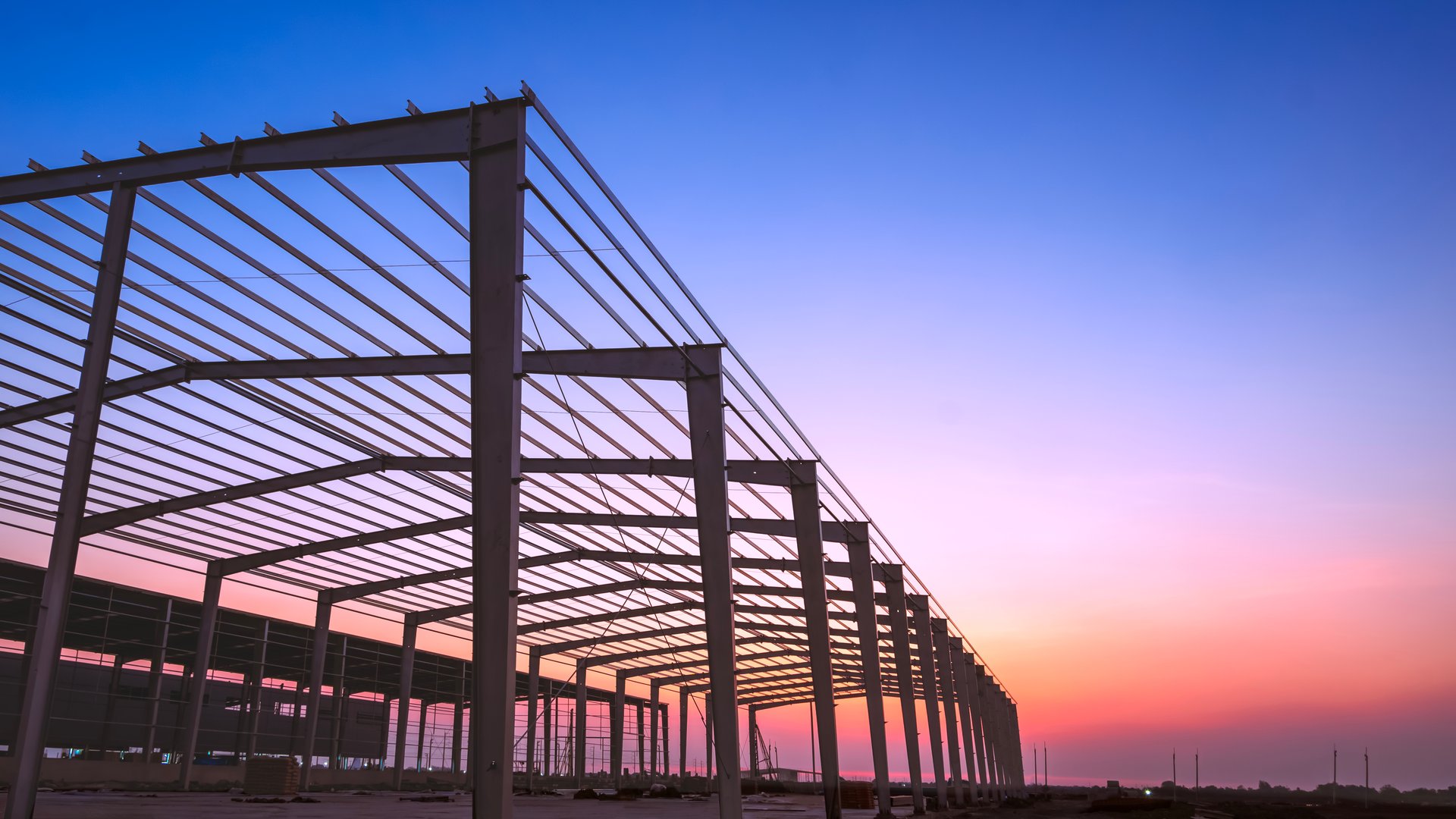 Silhouette industrial factory buildings framework with metal posts and roof beam structure in construction site against twilight sky background, Low angle and perspective side view