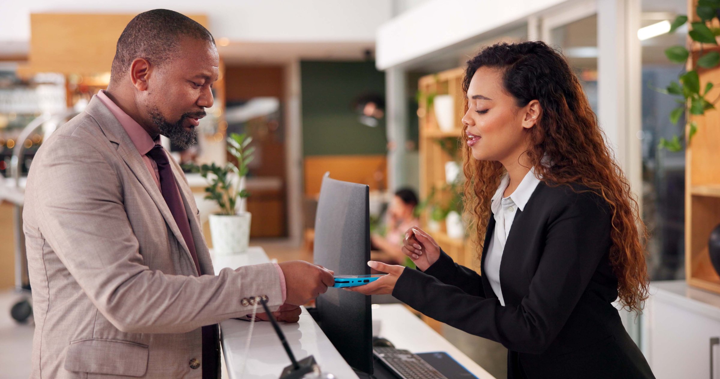 Hotel, receptionist and man with pay machine for booking, guest room service and reservation. Hospitality, front desk and person with concierge for pos payment, transaction and purchase in lobby