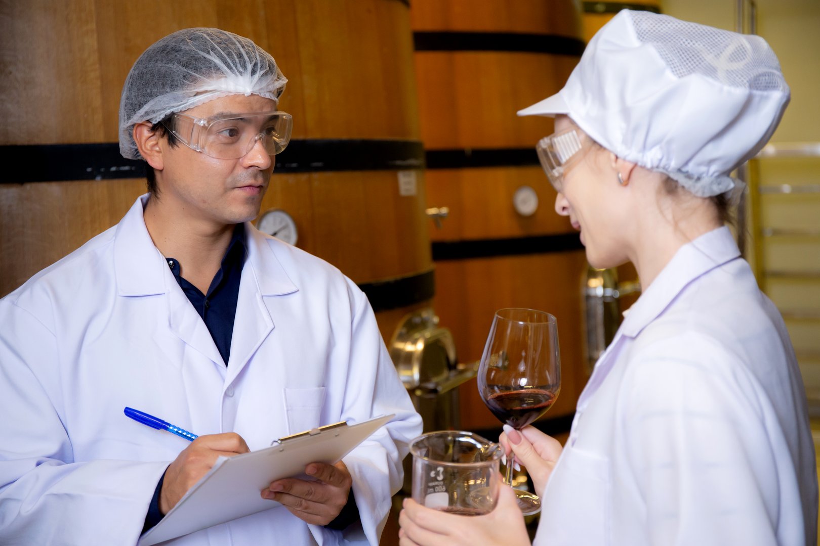 Winemaker team checking and examining producing wine at winery in factory, inspector checking quality and fermenting wine storage in tank or barrel at room, industrial and manufacture concept.