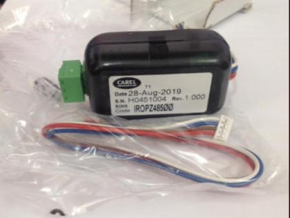 A small electronic device with a date label, serial number and colored wires, packaged in clear plastic.
