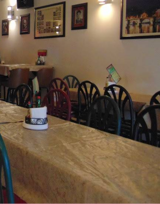 A restaurant dining area with empty tables and chairs, artwork on walls, and soft lighting creating a cozy atmosphere.