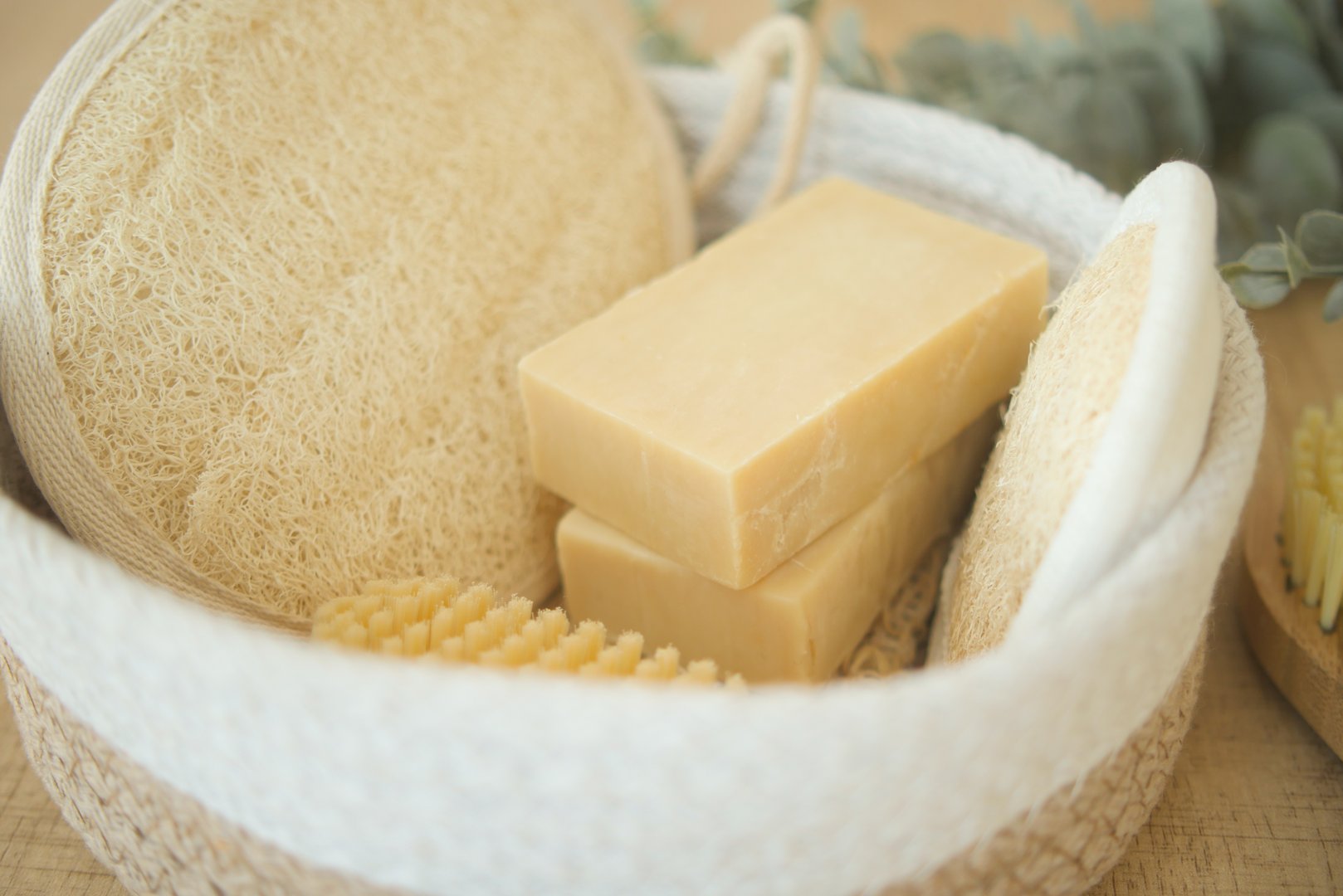 Natural spa set featuring soap bars, body brushes, loofah, and eucalyptus on a wooden surface.