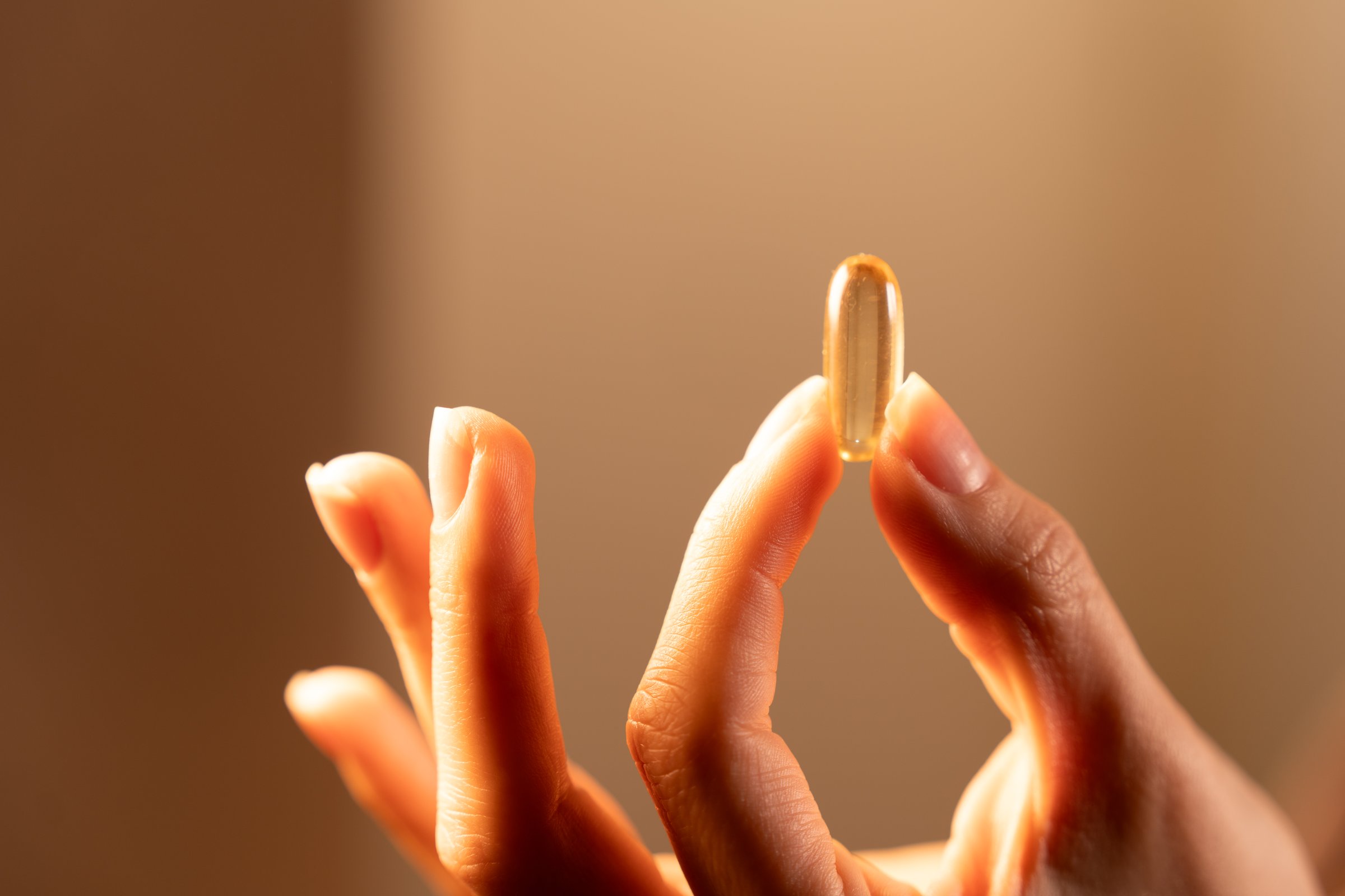 A person holds a clear gelatin capsule between their fingers, emphasizing the significance of omega 3 for health. The soft light creates a warm ambiance, focusing on the supplement.