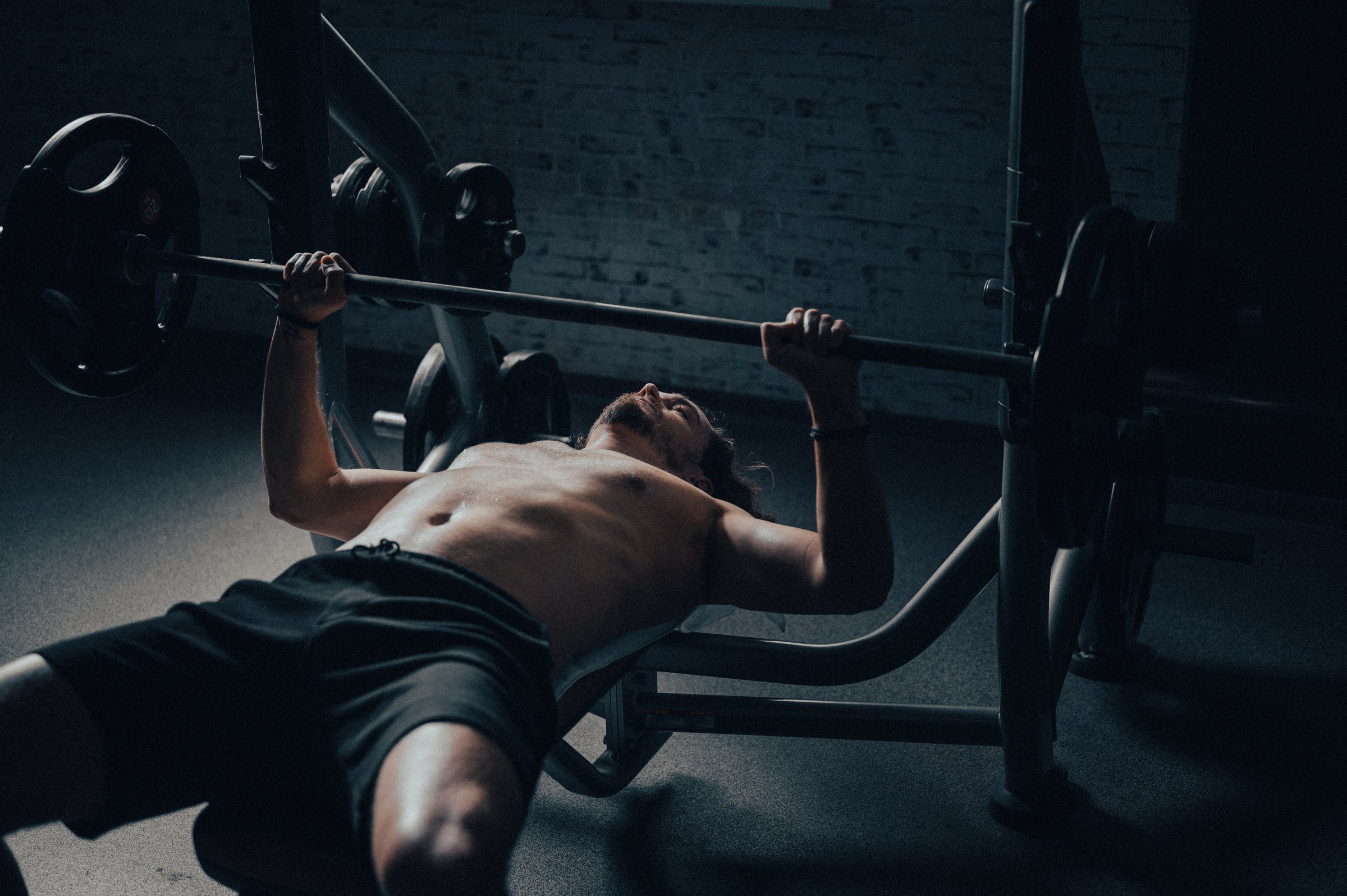 Close-up of a male athlete exercising bench press in a dark gym in strong side light