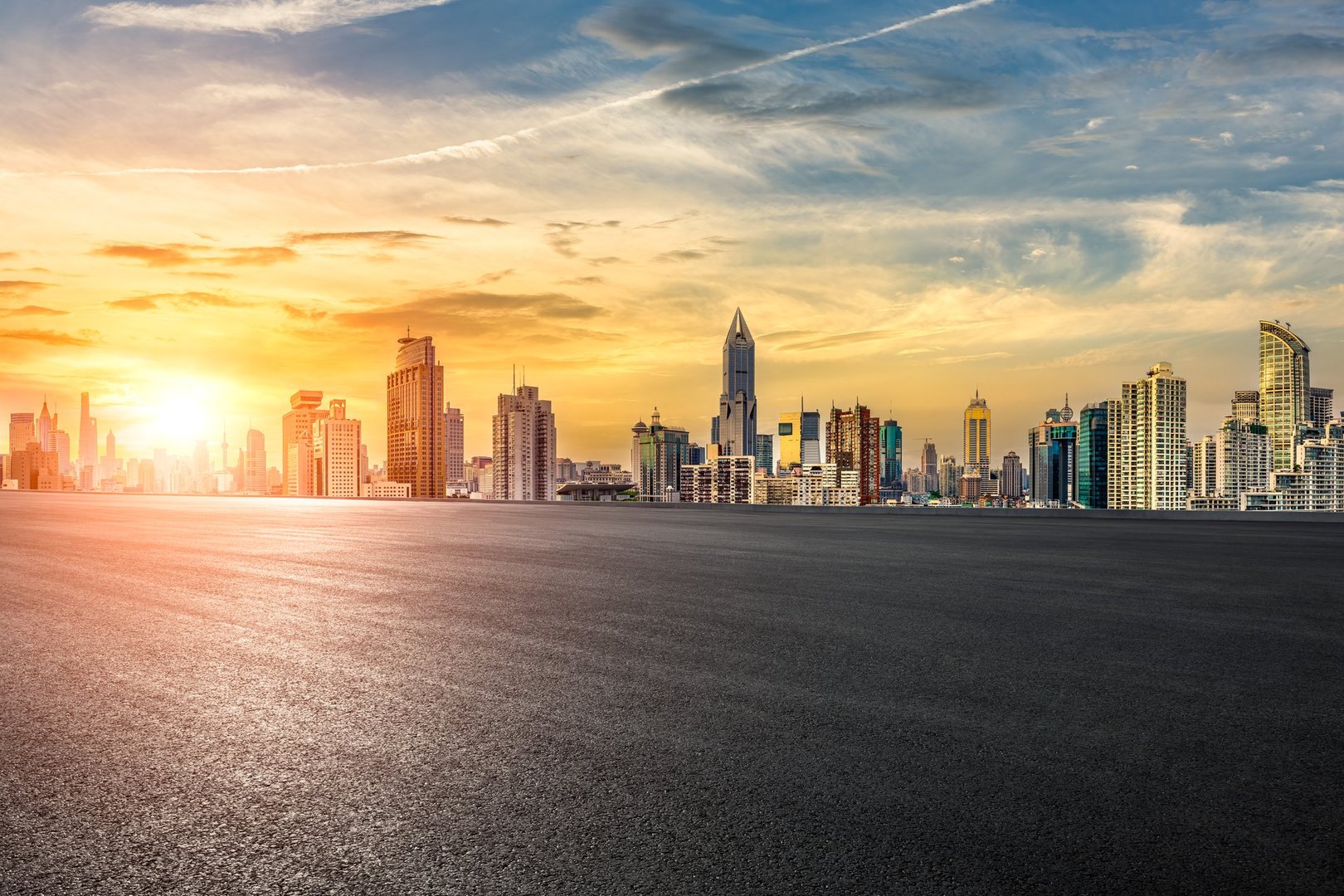Empty asphalt road leads through a cityscape with an impressive skyline at sunset, offering potential for transportation.