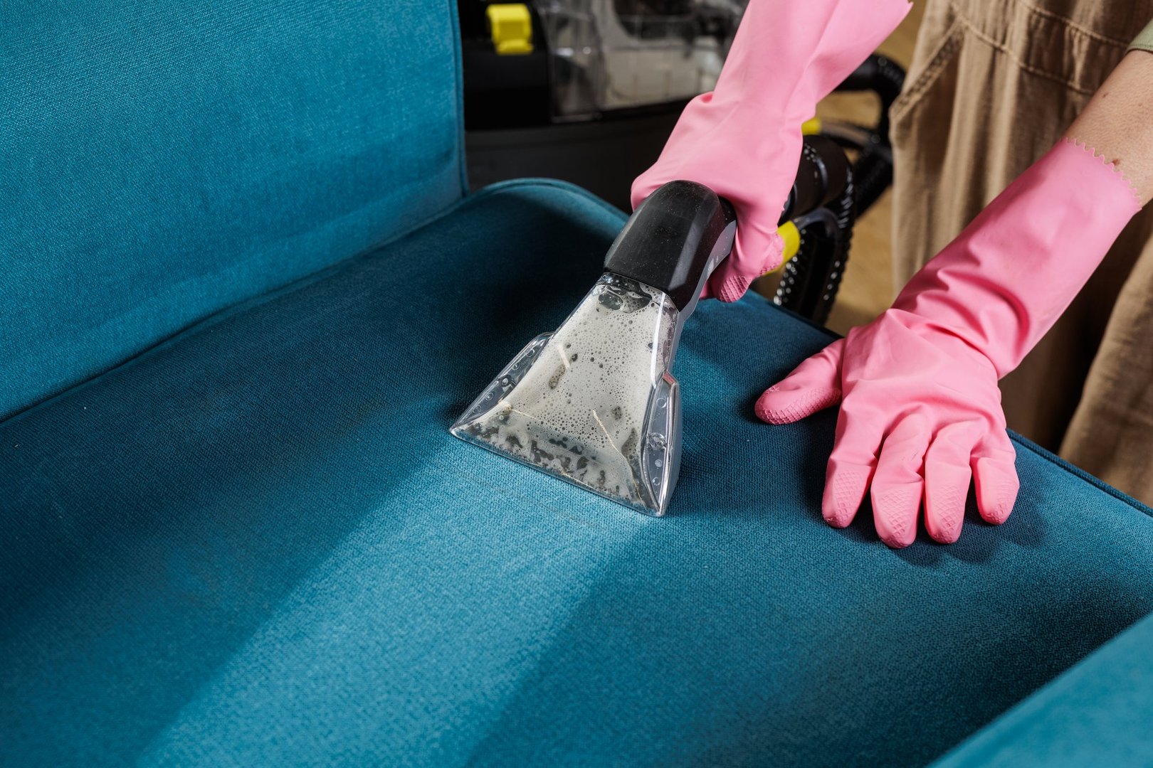 Female worker in rubber gloves wet vacuums blue upholstered chair seat during professional home stain removal service