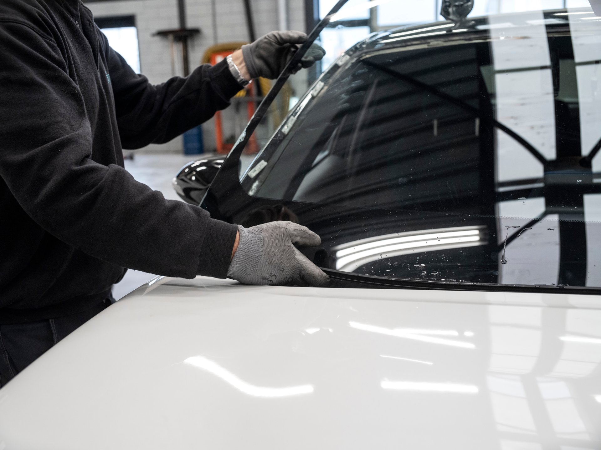 Mechanic performing windshield installation or repair work on vehicle in professional automotive service environment