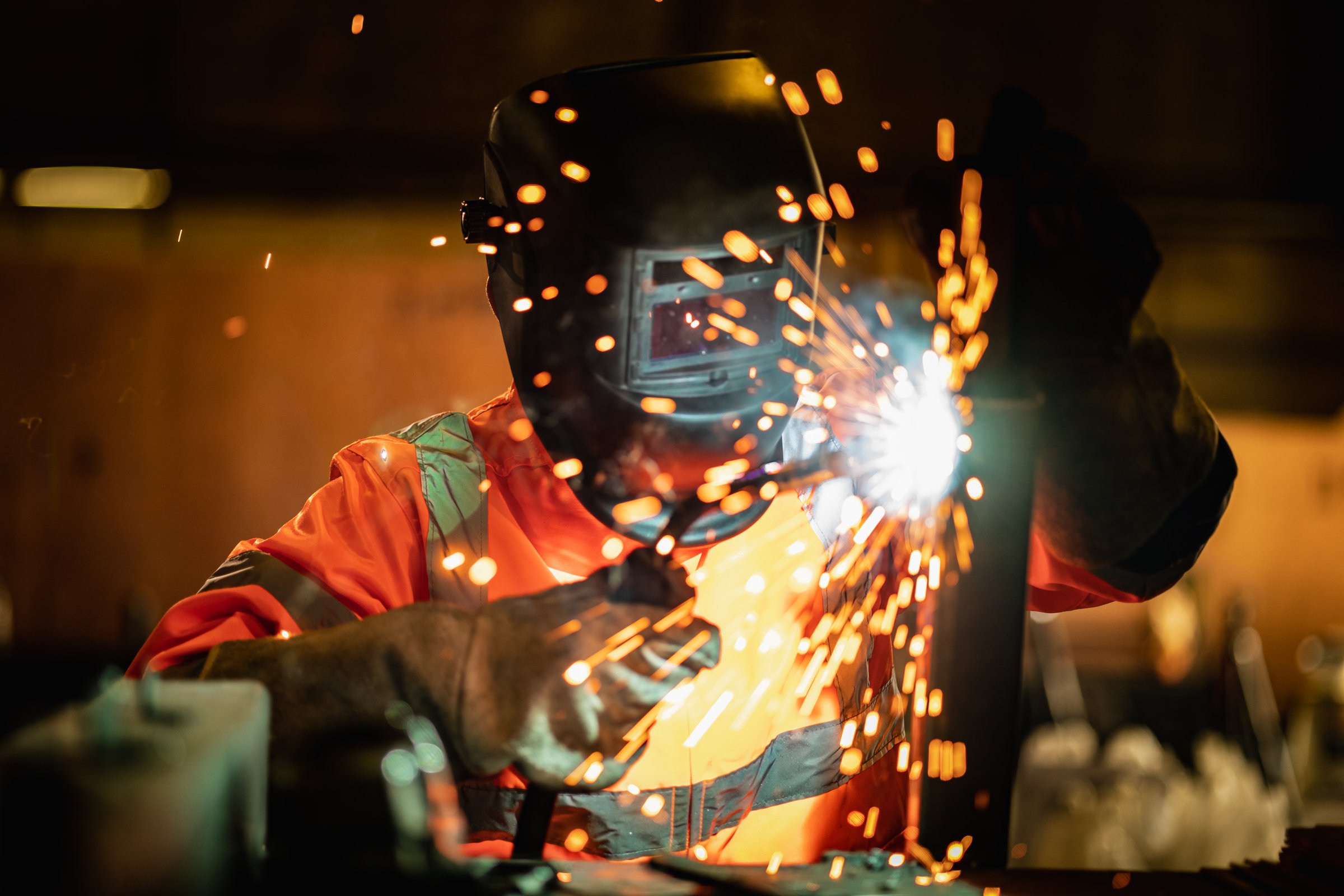 Closeup workers wearing industrial uniforms and using electric arc welding machine to weld steel at factory. Metalwork manufacturing and construction maintenance service by manual skill labor concept.
