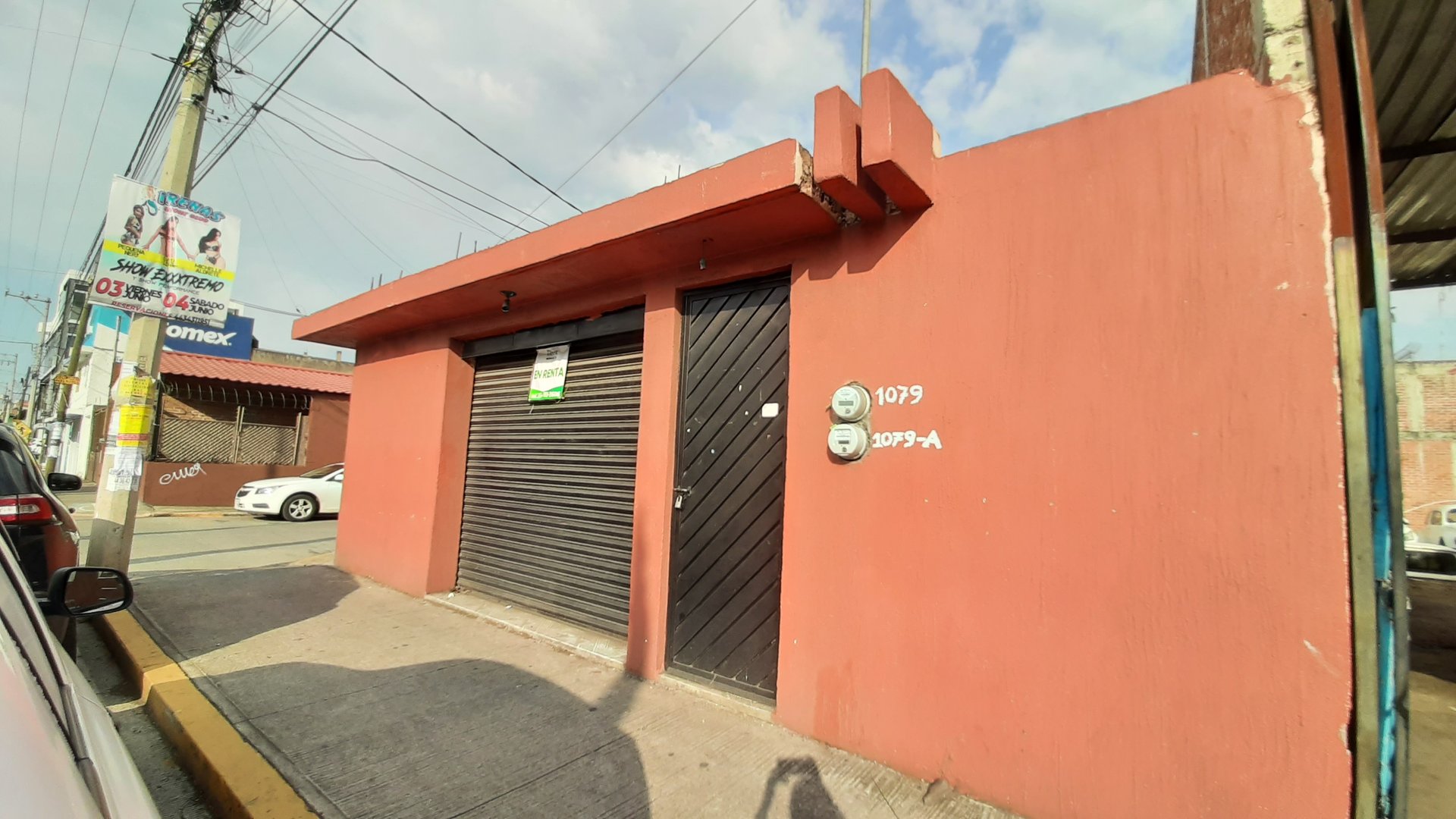 Red building with black garage doors, numbered 1079 and 1079-A, on a sidewalk with wires overhead.