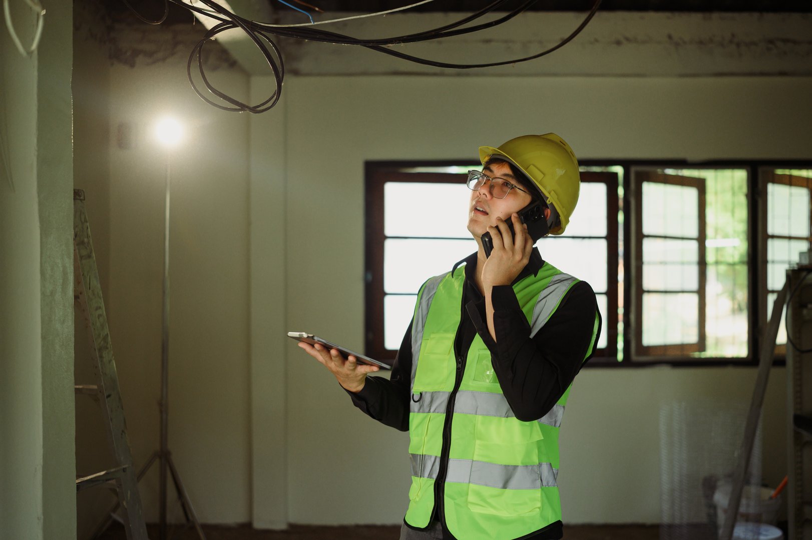Construction manager on phone call while inspecting ceiling wiring during renovation project.