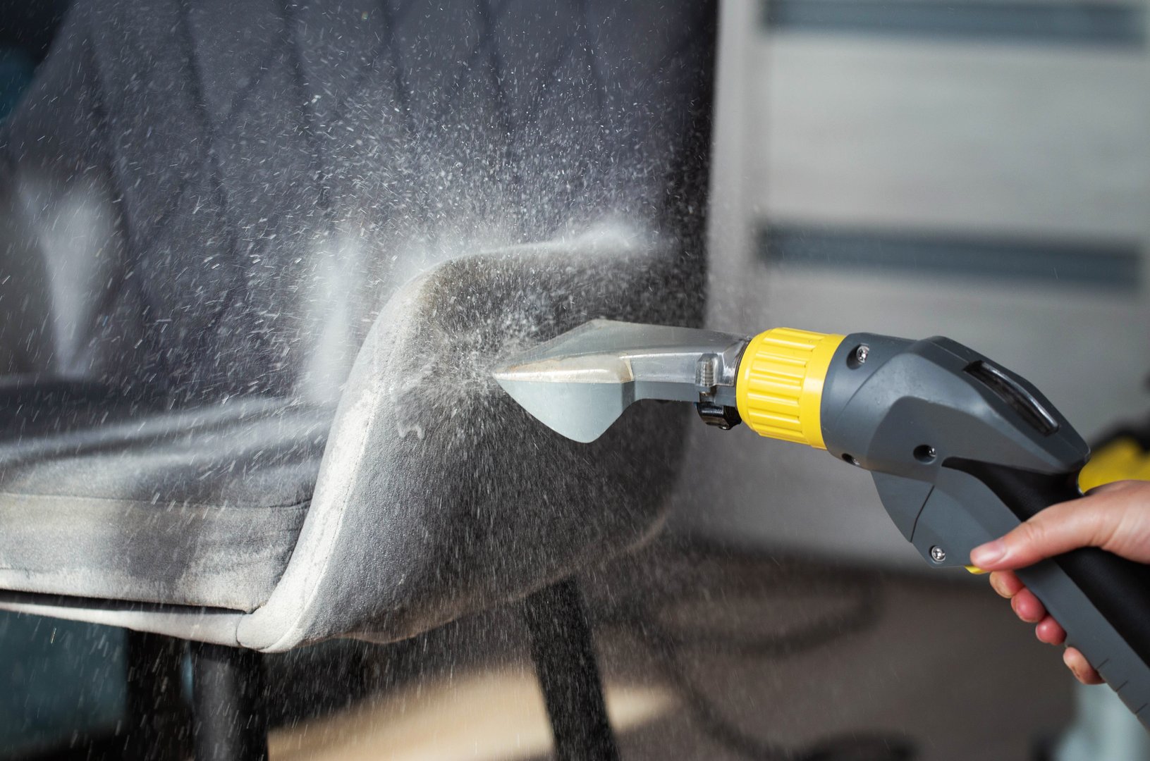 Spraying a chemical from a washing vacuum cleaner when cleaning the fabric upholstery of a chair. Cleaning services