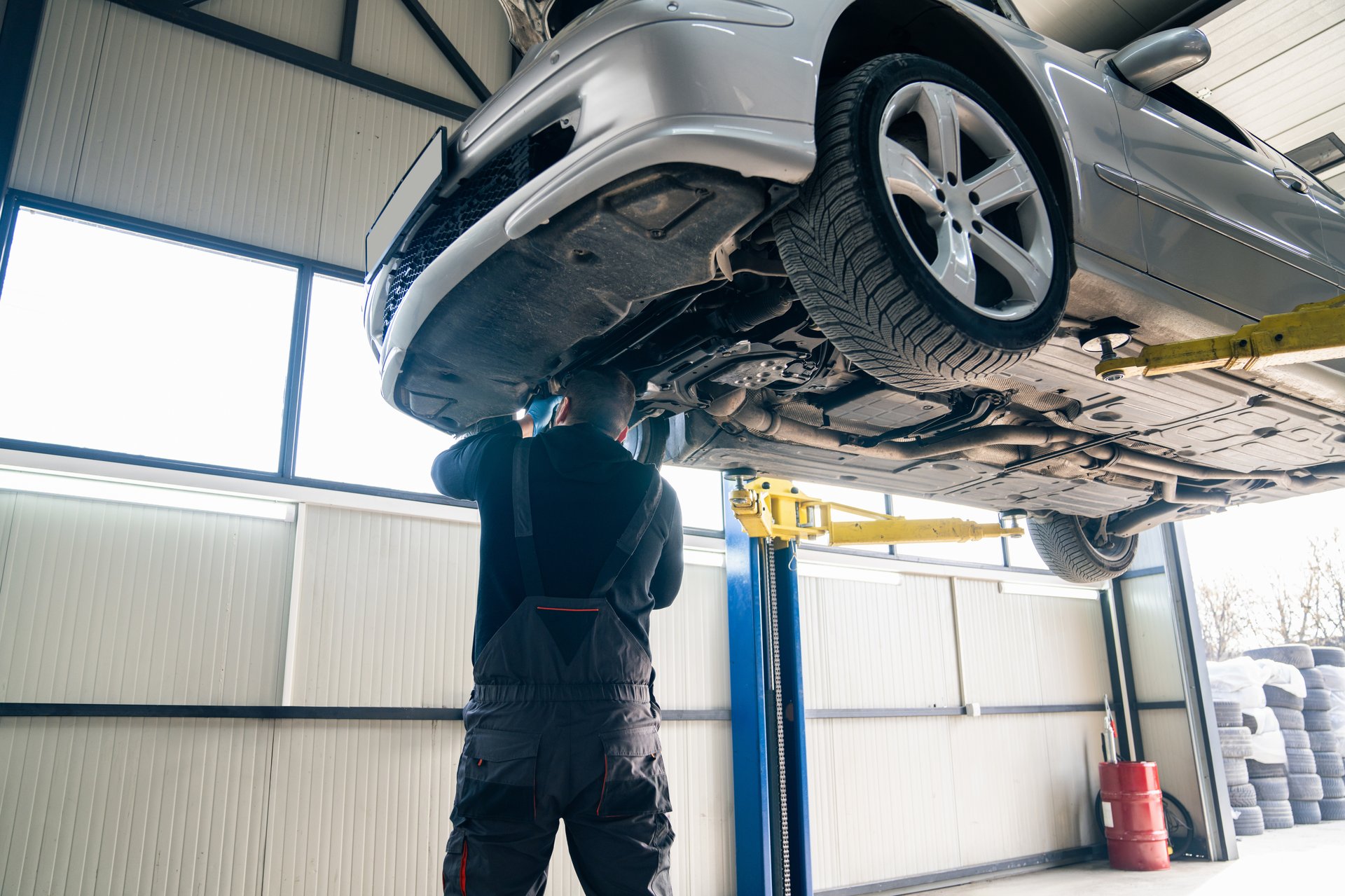 Serviceman checks car suspension on a column lift in car service. Car repair in car service. Car with opened car hood on a lift in a car service.