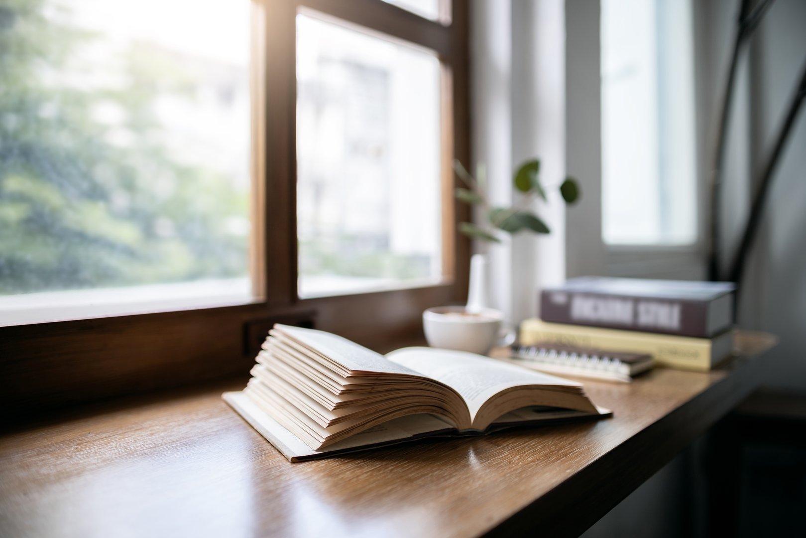 An open book for reading and relaxing with coffee drink on wooden table by the window in cafe