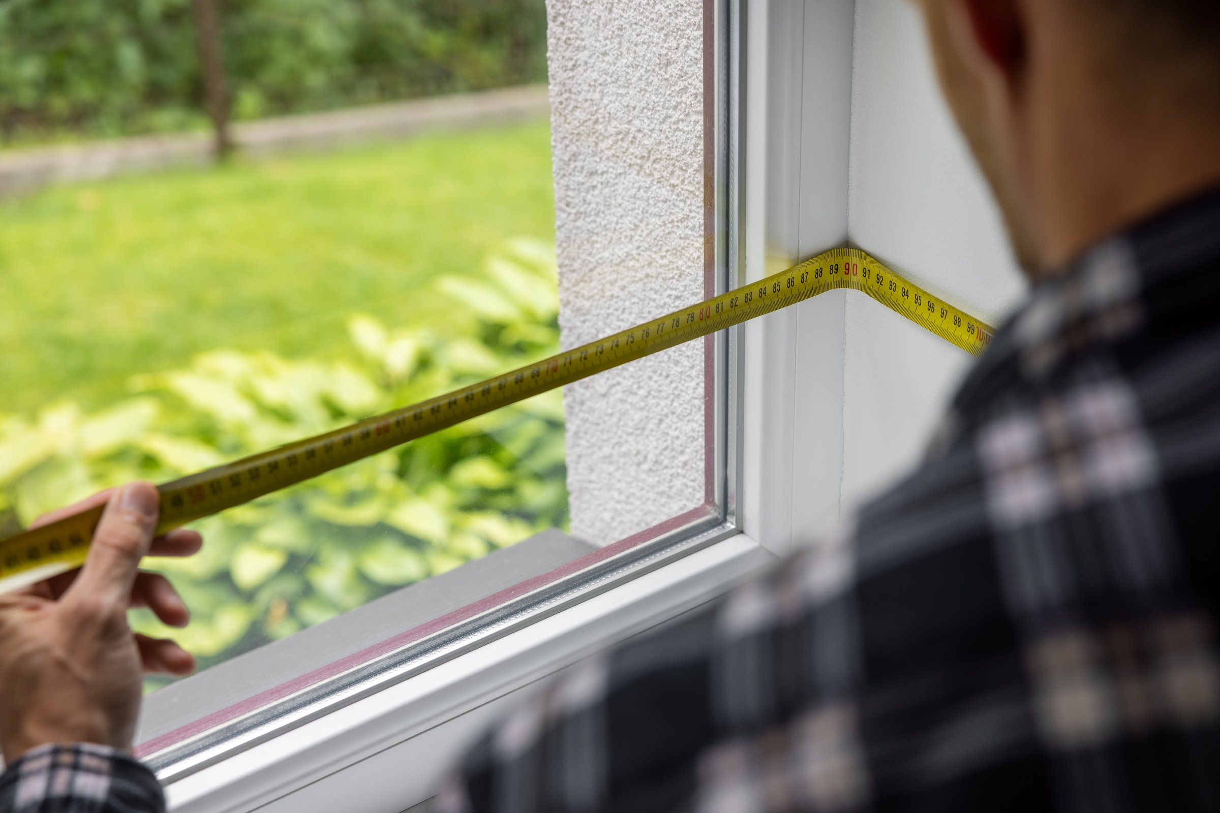 man measuring white plastic window frame for replace