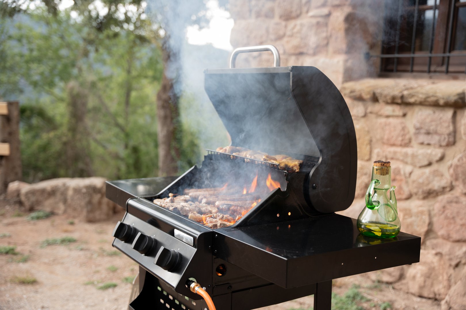Open barbecue grill with smoke and fire cooking meat in a backyard patio.