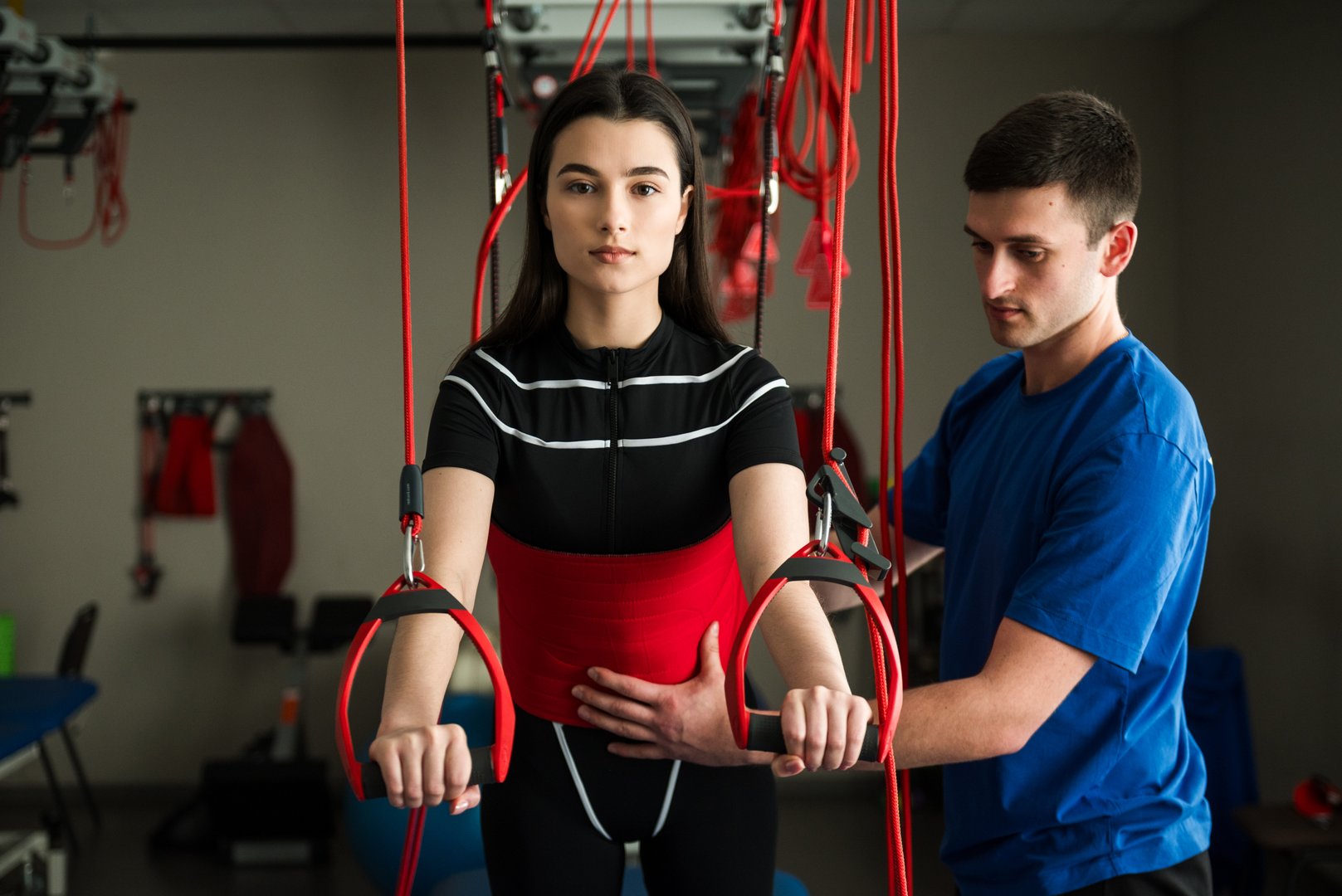 Pain-free red cord treatment of sport injury. Activating neuromuscular system with red rope equipment. Girl is going through supervised red cord physiotherapy at rehabilitation center