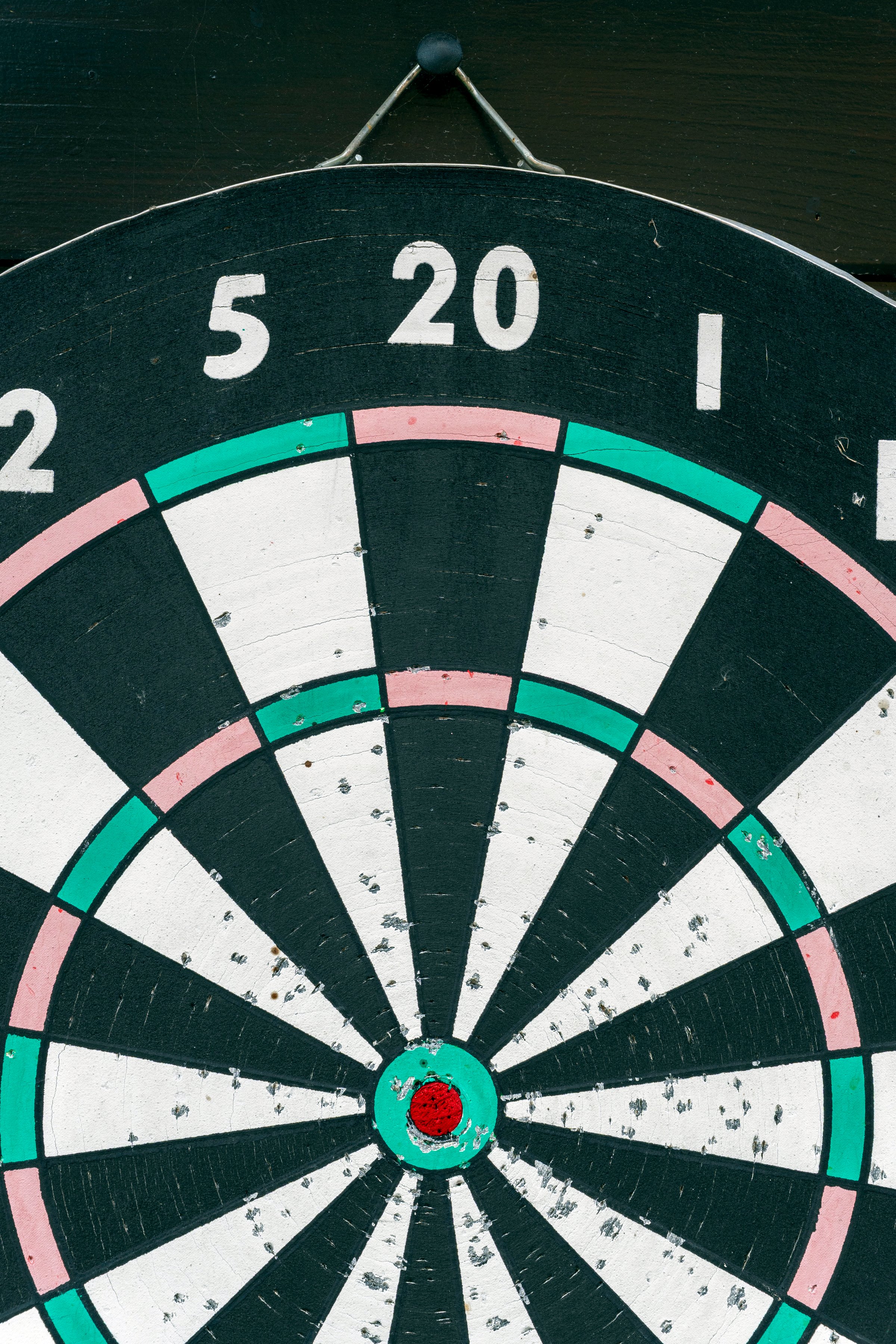 A well-worn darts board features clear scoring sections in black, white, and green colors. Marks from previous games are visible, highlighting its frequent use in a casual setting.
