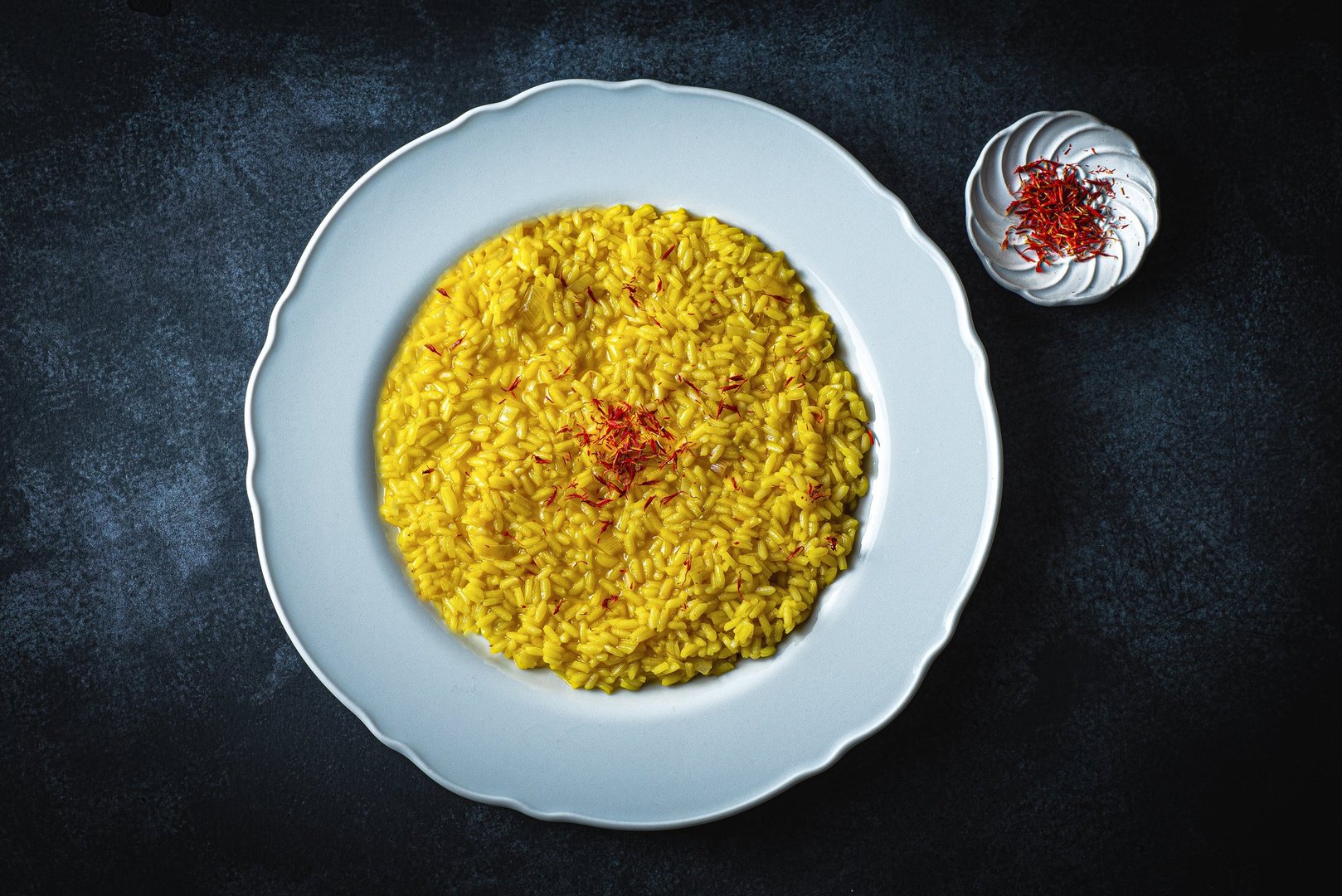 Risotto Milanese in a white aristocratic dish on the dark table. A classic Lombard saffron risotto recipe. Cuisine the North Italy, dark key