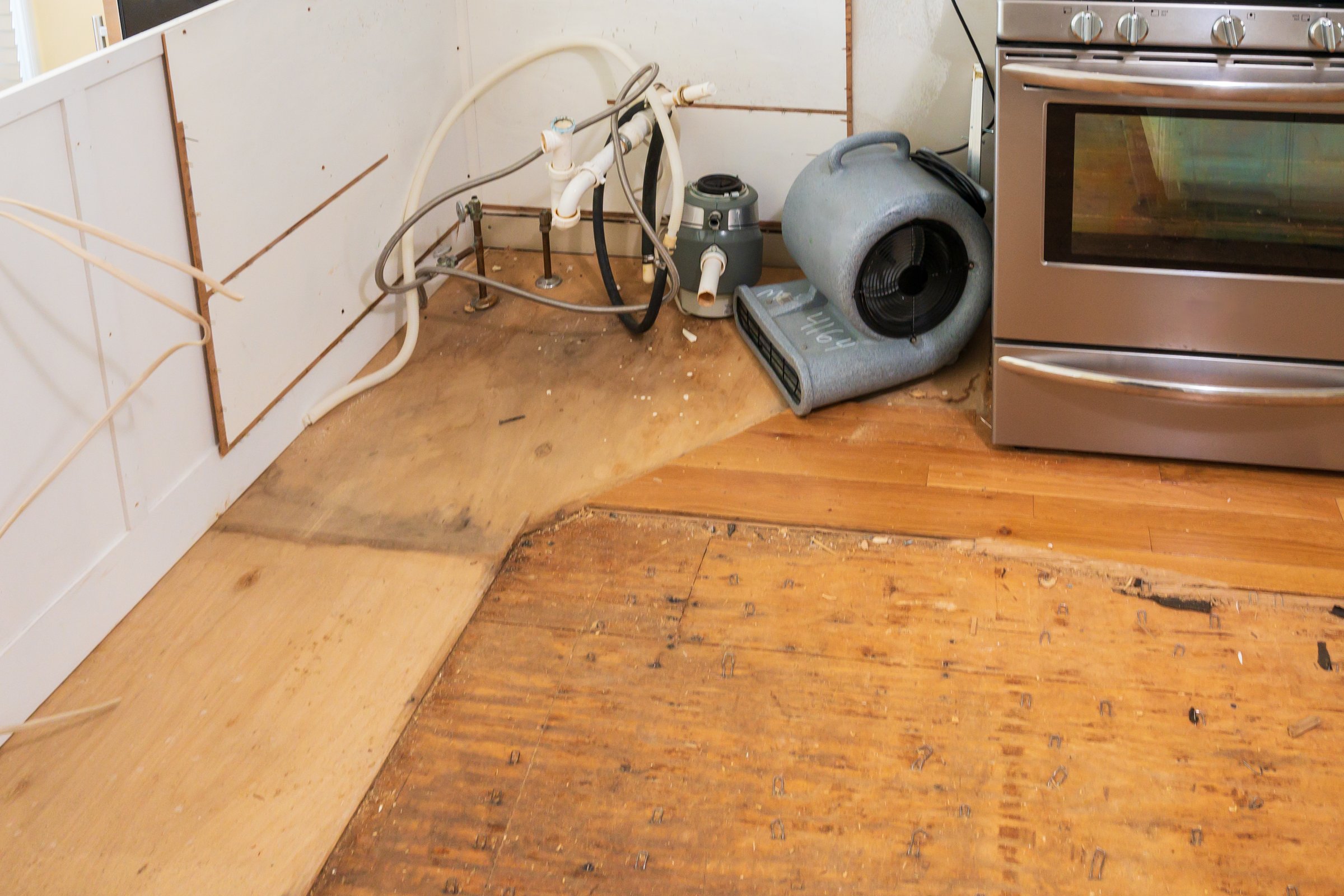 Hardwood floor pulled up after water damage with damage to adjacent kitchen cabinets.