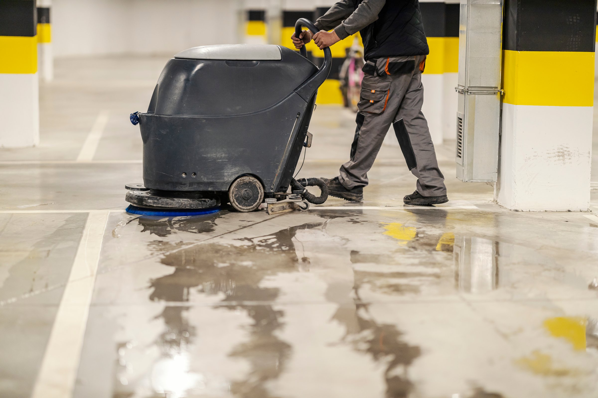 Side view of unrecognizable worker washing garage parking with washing machine.