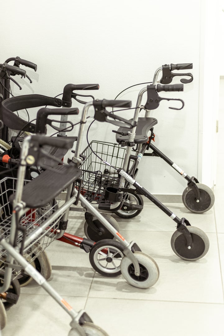 Several mobility walkers are neatly arranged in a bright healthcare facility. The environment is clean, with strong natural light illuminating the space.