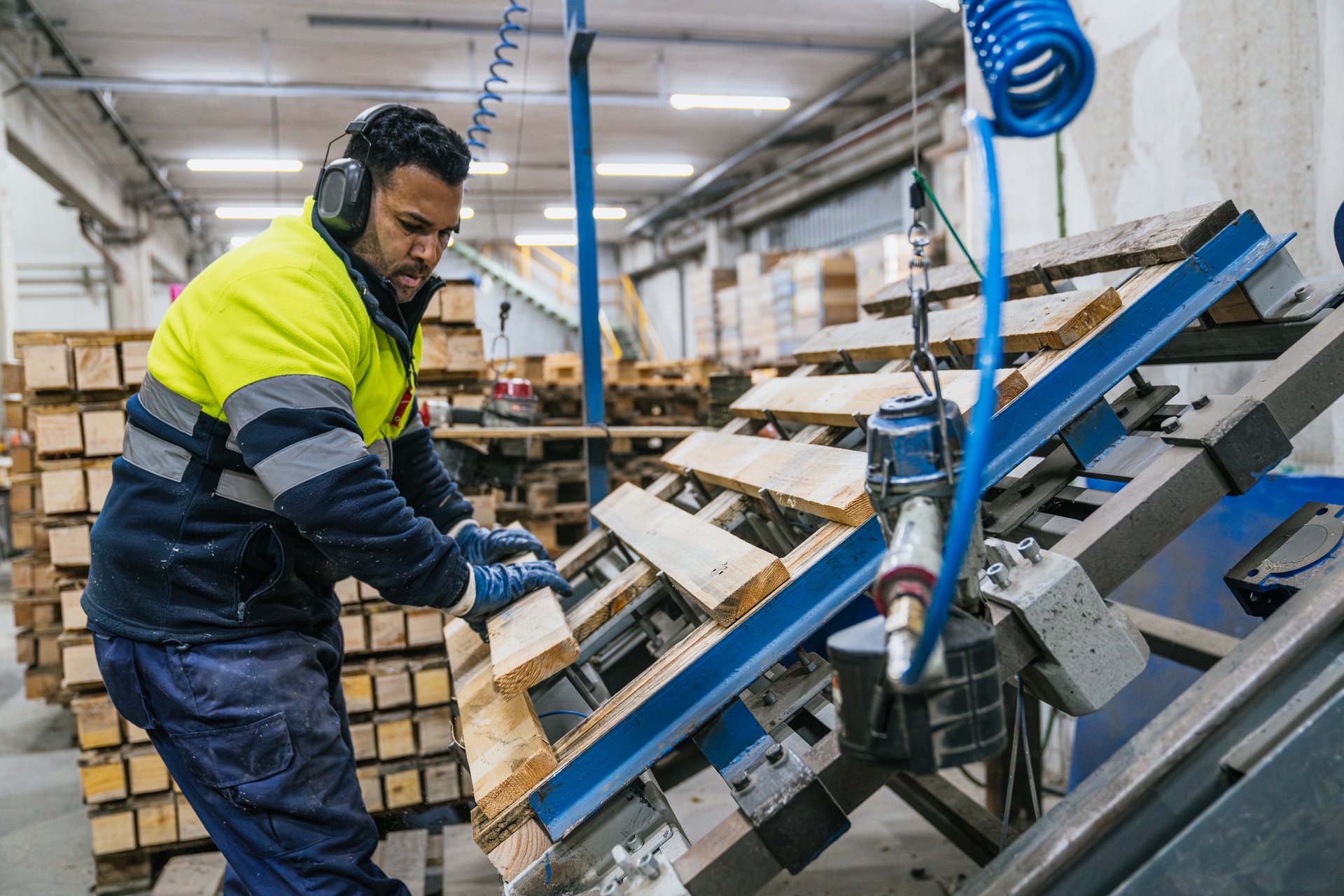 Carpenter assembling wooden pallets in a recycling factory, wearing safety equipment and using specialized tools