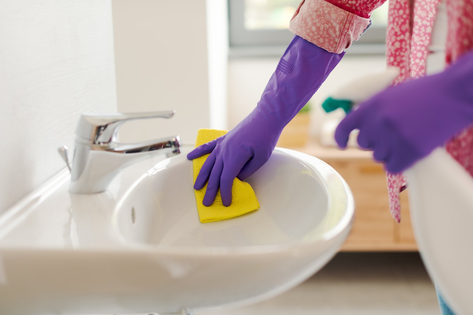 Housewife cleaning the bathroom, she is disinfecting the sink using a spray detergent, hands close up